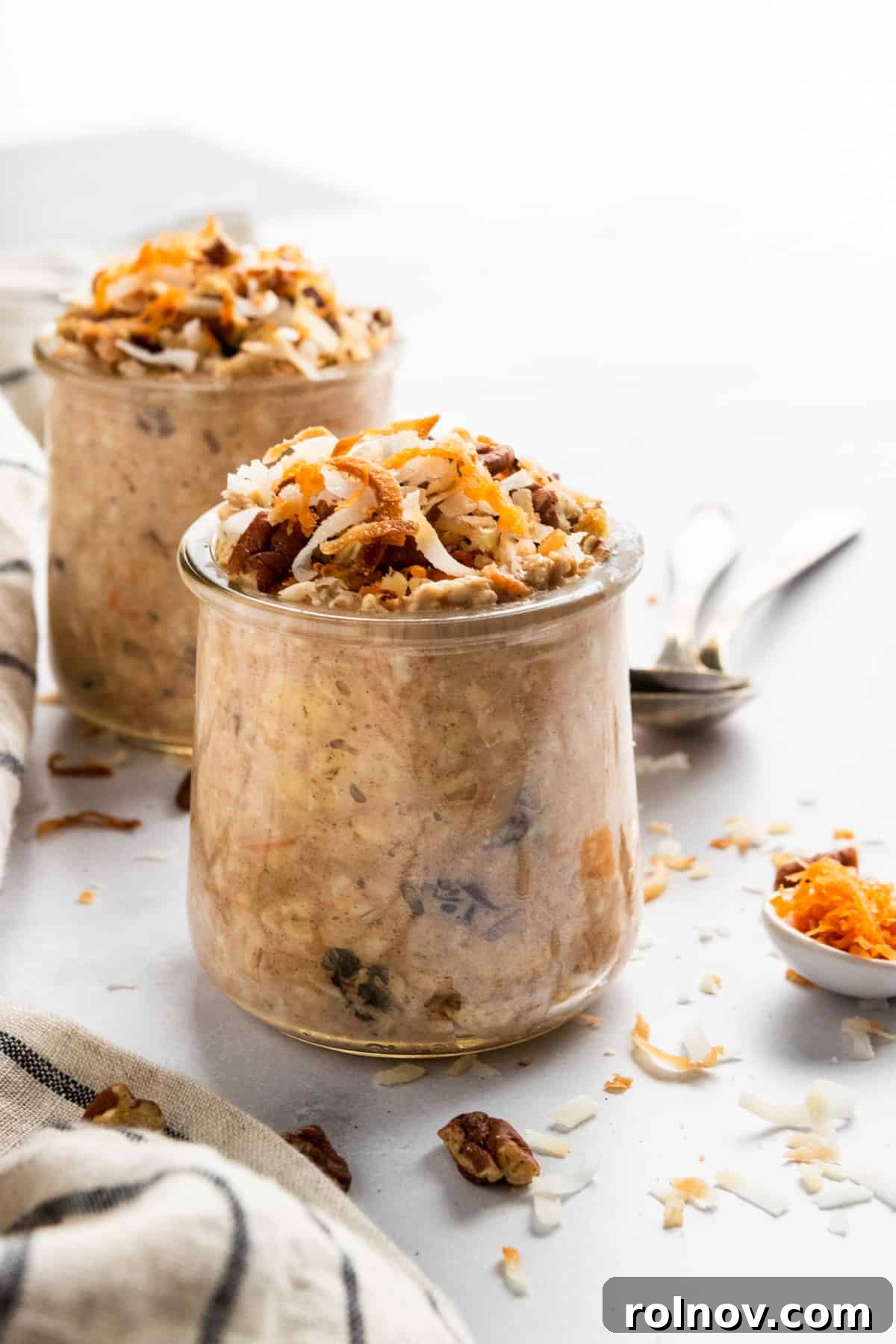 Spiced Carrot Cake Overnight Oats 2 Overnight Oatmeal in jars with a spoonful of shredded carrot, cinnamon, and coconut flakes, showcasing a delightful breakfast.