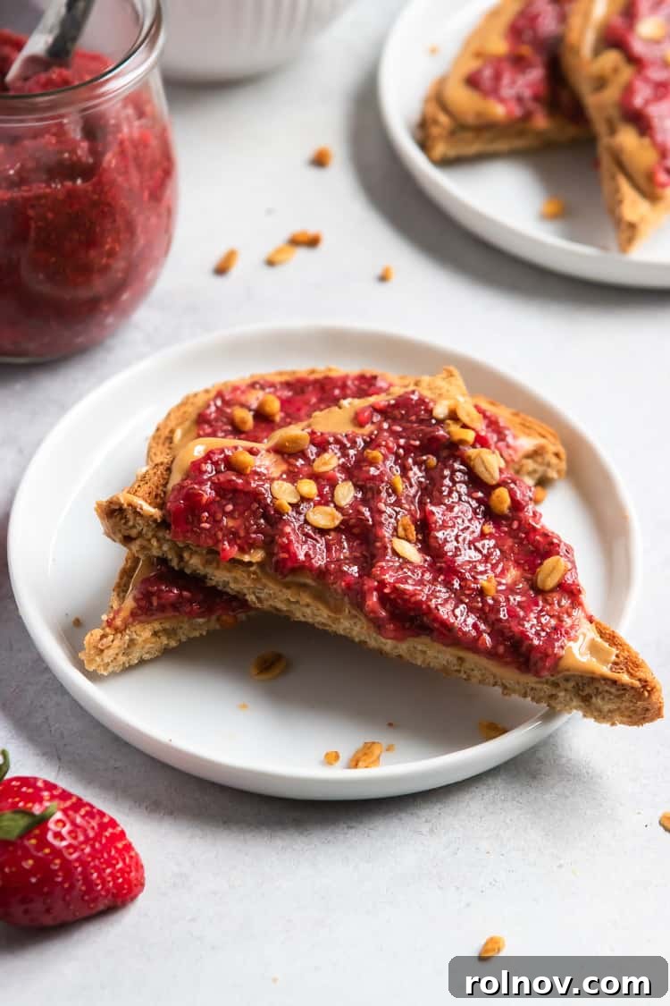 Freshly made strawberry chia jam spread on peanut butter toast slices on a white plate, highlighting its vibrant color and chunky texture.