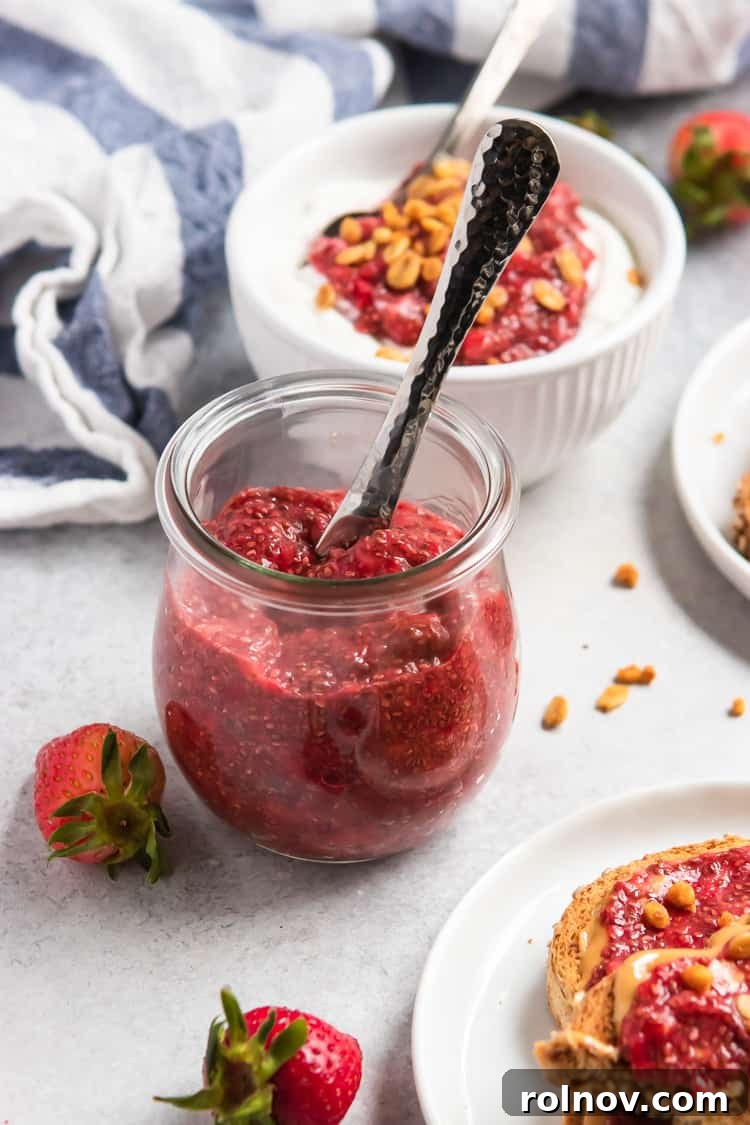 A glass jar filled with vibrant homemade vegan strawberry chia jam, accompanied by fresh strawberries and a knife.