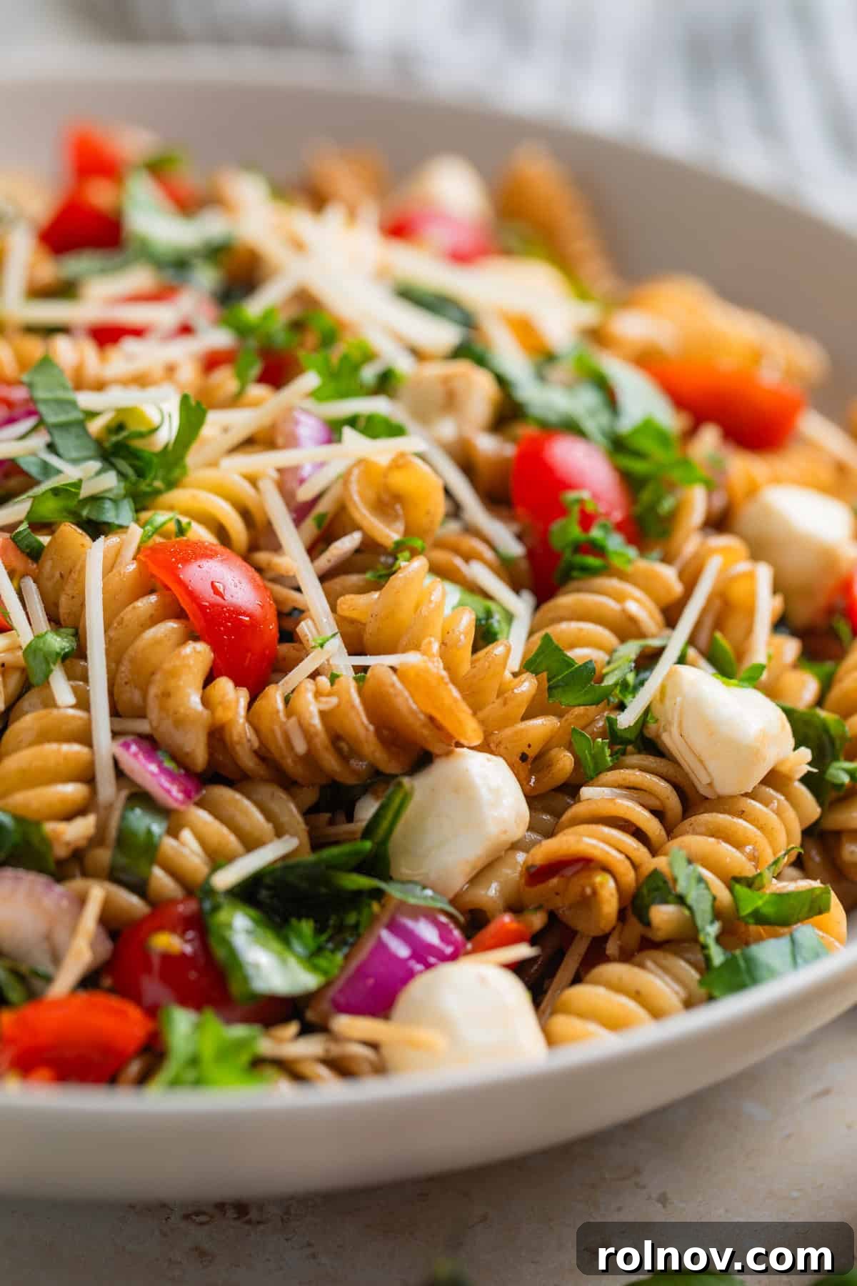 Sun-Kissed Tomato Basil Pasta Salad 12 Close up view of tomato and basil rotini pasta salad topped with shredded parmesan and chopped basil.