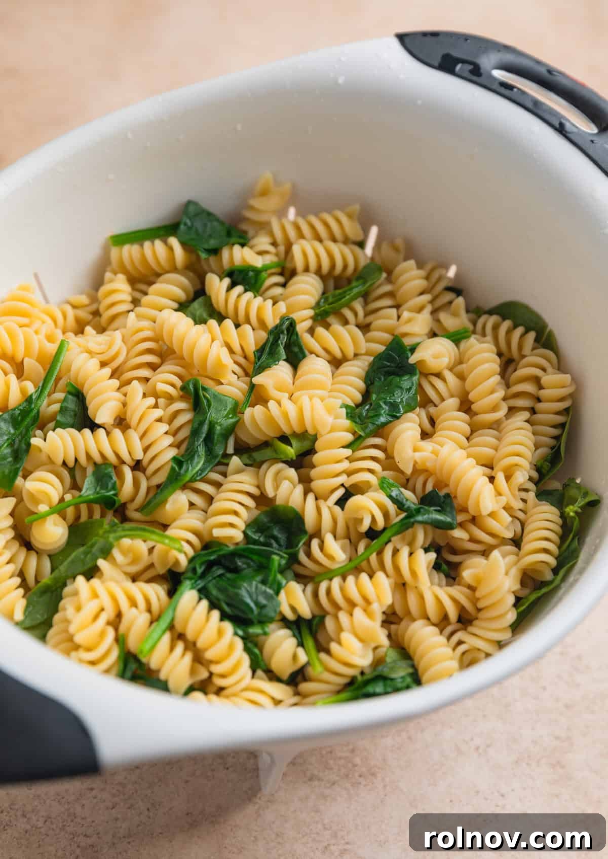 Sun-Kissed Tomato Basil Pasta Salad 4 Cooked rotini pasta in colander with wilted spinach.