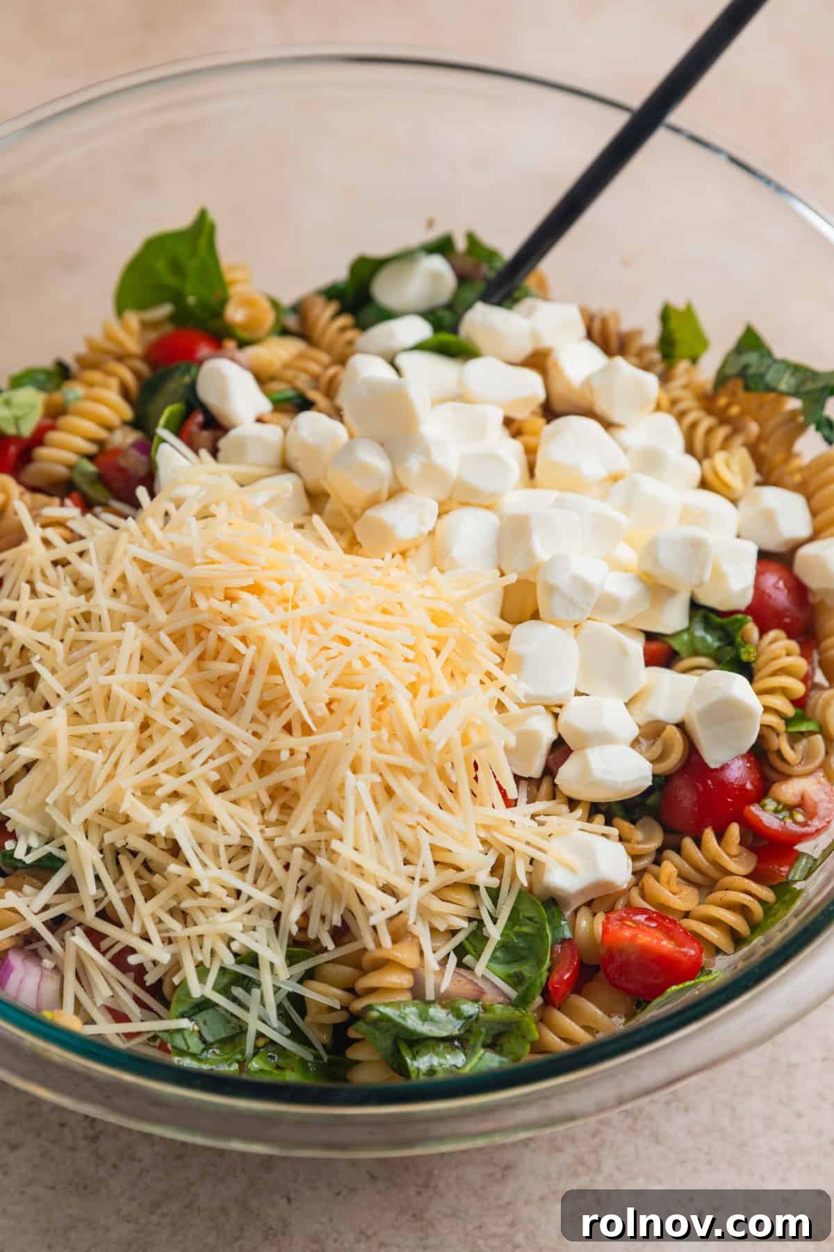 Sun-Kissed Tomato Basil Pasta Salad 9 Shredded parmesan and fresh mozzarella pearls on top of rotini and vegetable mixture in bowl.