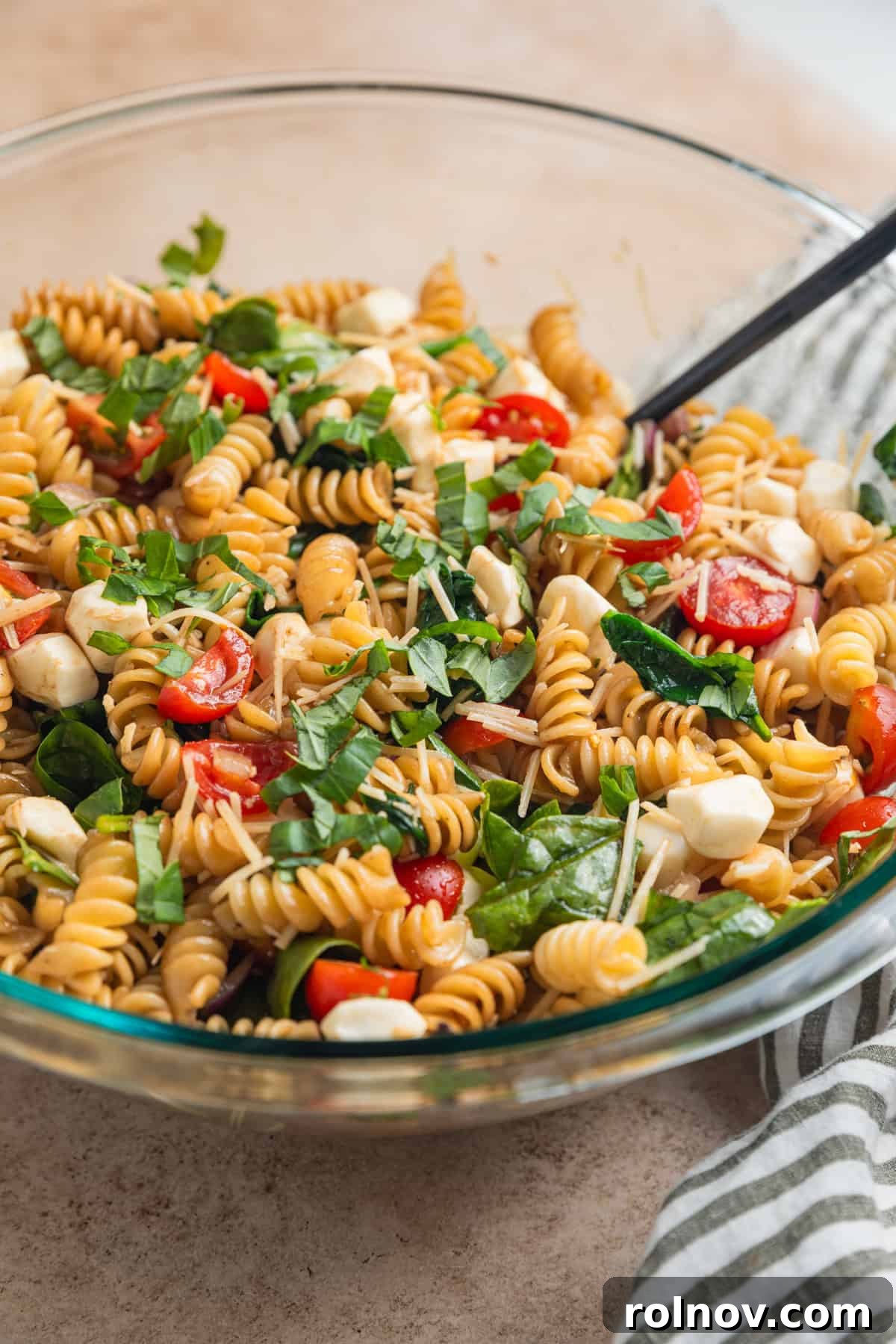 Sun-Kissed Tomato Basil Pasta Salad 10 Prepped pasta salad with basil, tomatoes, mozzarella, spinach and other ingredients in bowl.