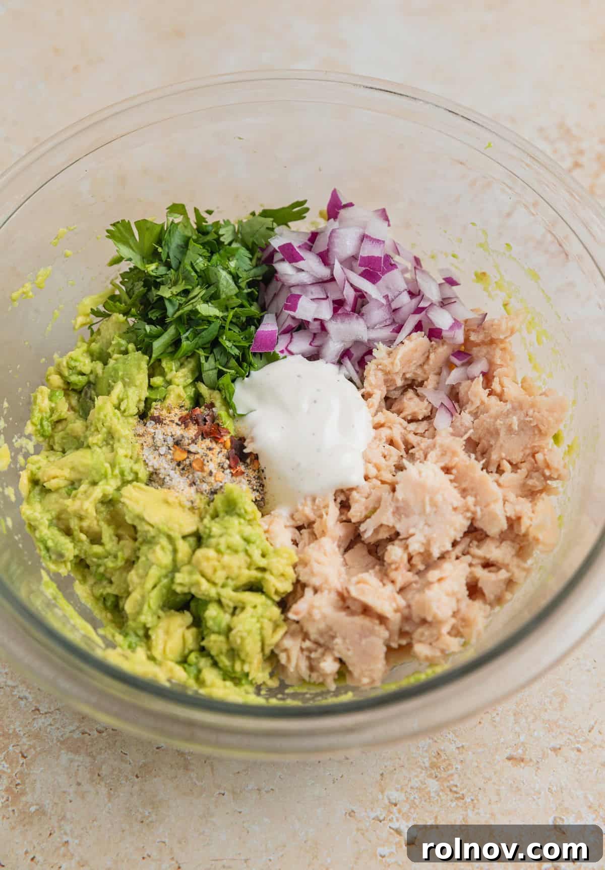 Creamy Avocado Ranch Tuna Salad 5 Flaked tuna, red onion, cilantro, avocado and Ranch dressing in mixing bowl before being stirred.