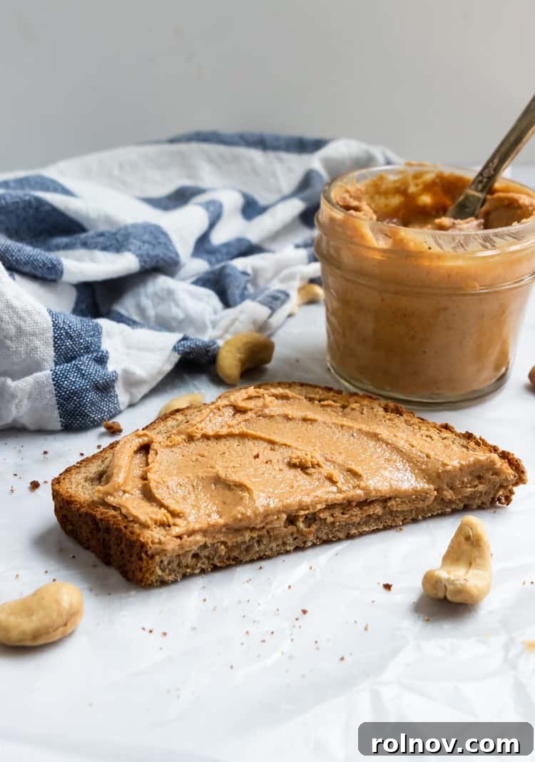 Silky Smooth Maple Vanilla Cashew Butter 3 Close-up of creamy Maple Vanilla Cashew Butter in a jar with cashews scattered around.
