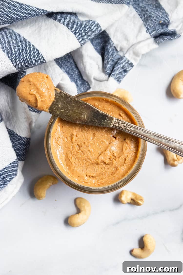 Silky Smooth Maple Vanilla Cashew Butter 5 A jar of homemade Maple Vanilla Cashew Butter with a spoon, next to some whole cashews.