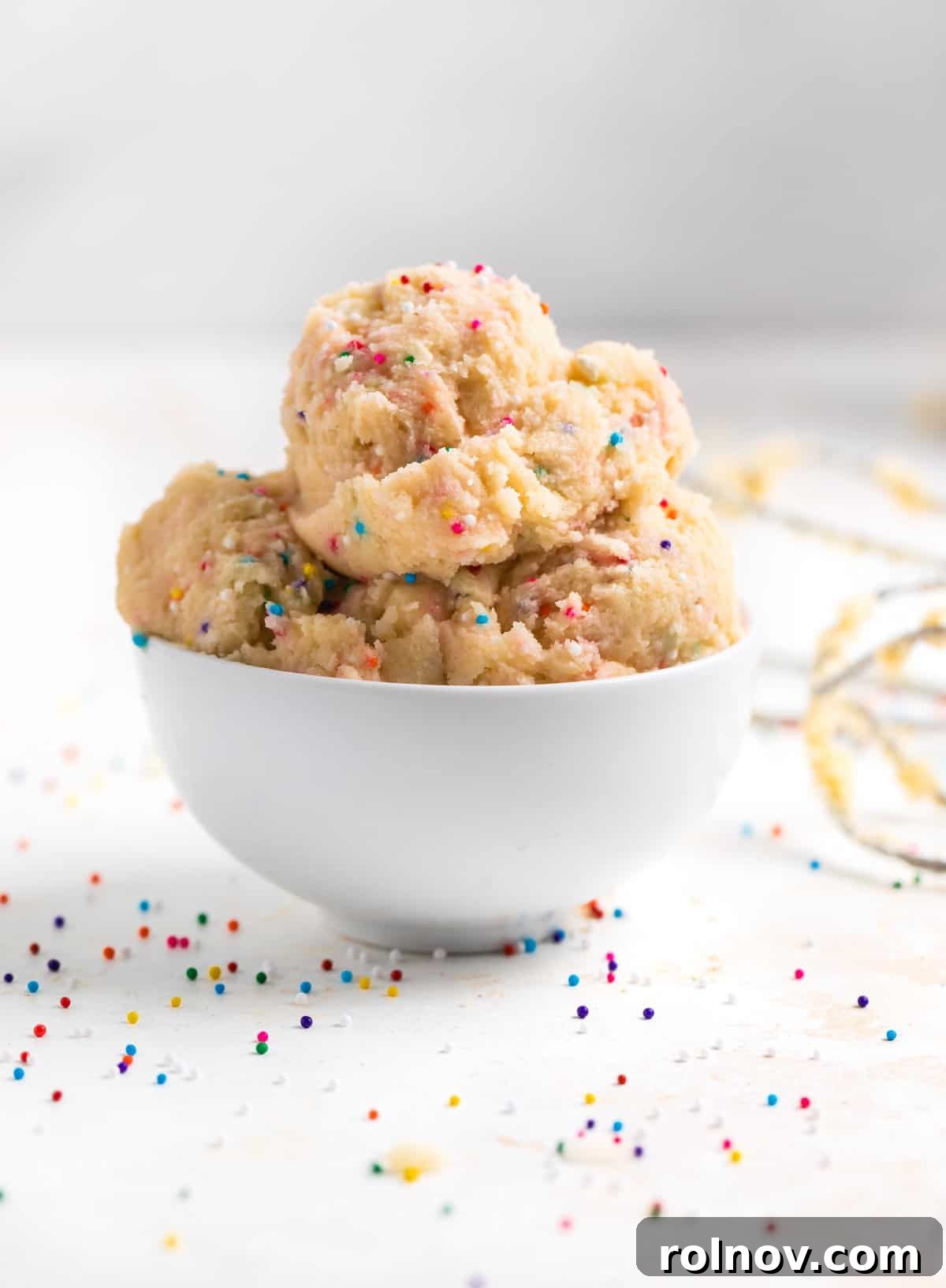 Spoonable Sugar Cookie Dough 6 A white bowl brimming with perfectly scooped edible sugar cookie dough, adorned with vibrant funfetti sprinkles, ready for a delightful indulgence.