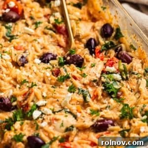 Creamy feta baked chicken and orzo topped with olives, parsley and basil in pan.