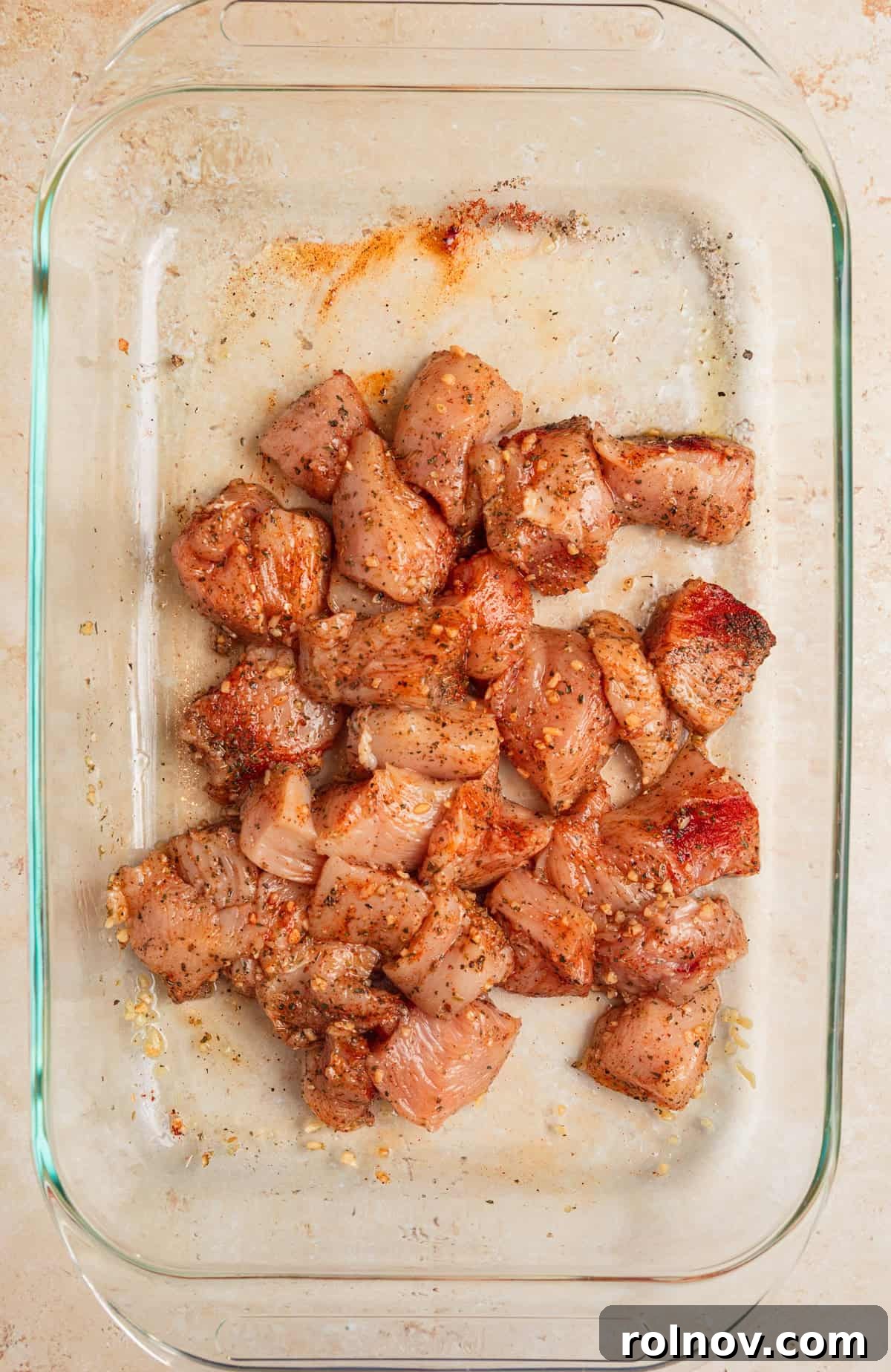 Aegean Chicken and Orzo Bake 5 Cubed chicken breast pieces in a baking pan, coated evenly with olive oil and a blend of Greek spices like oregano, basil, salt, and pepper, ready for baking.