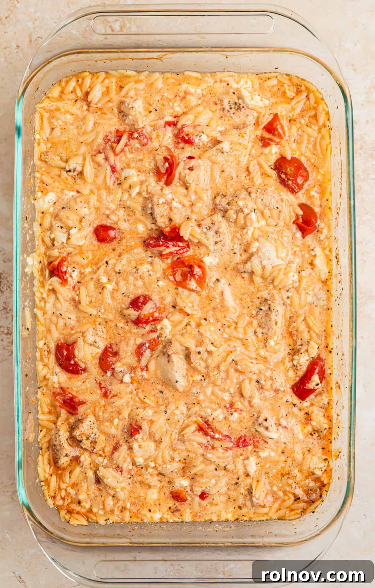 Aegean Chicken and Orzo Bake 8 A close-up of the baked Greek chicken and orzo in a glass dish, after stirring in the melted feta cheese and burst tomatoes, creating a wonderfully creamy and rustic texture.