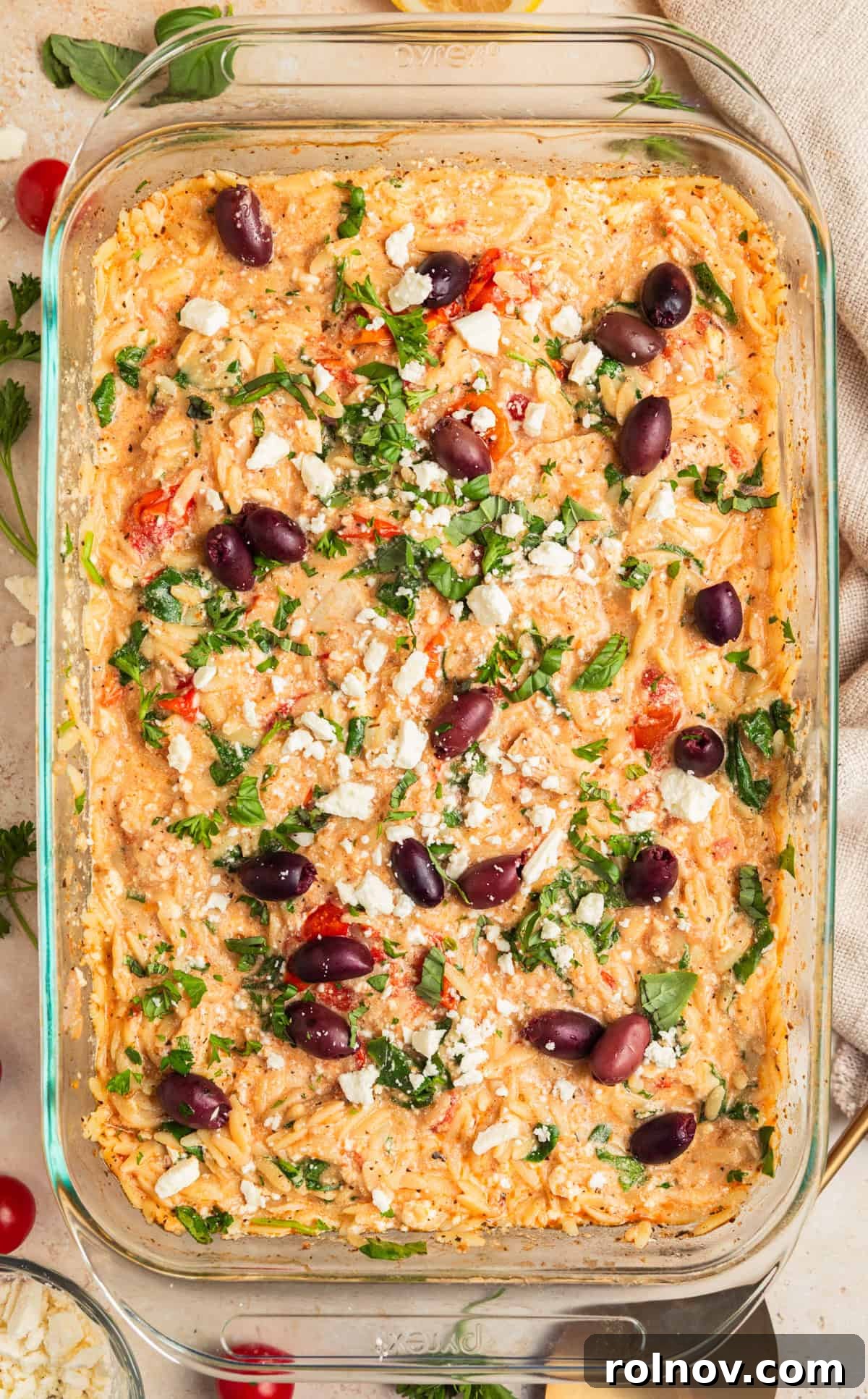 Aegean Chicken and Orzo Bake 10 A beautifully finished Greek chicken and orzo bake, garnished with additional feta cheese crumbles, shiny Kalamata olives, and fresh parsley, presented in a glass baking dish, ready to be served.
