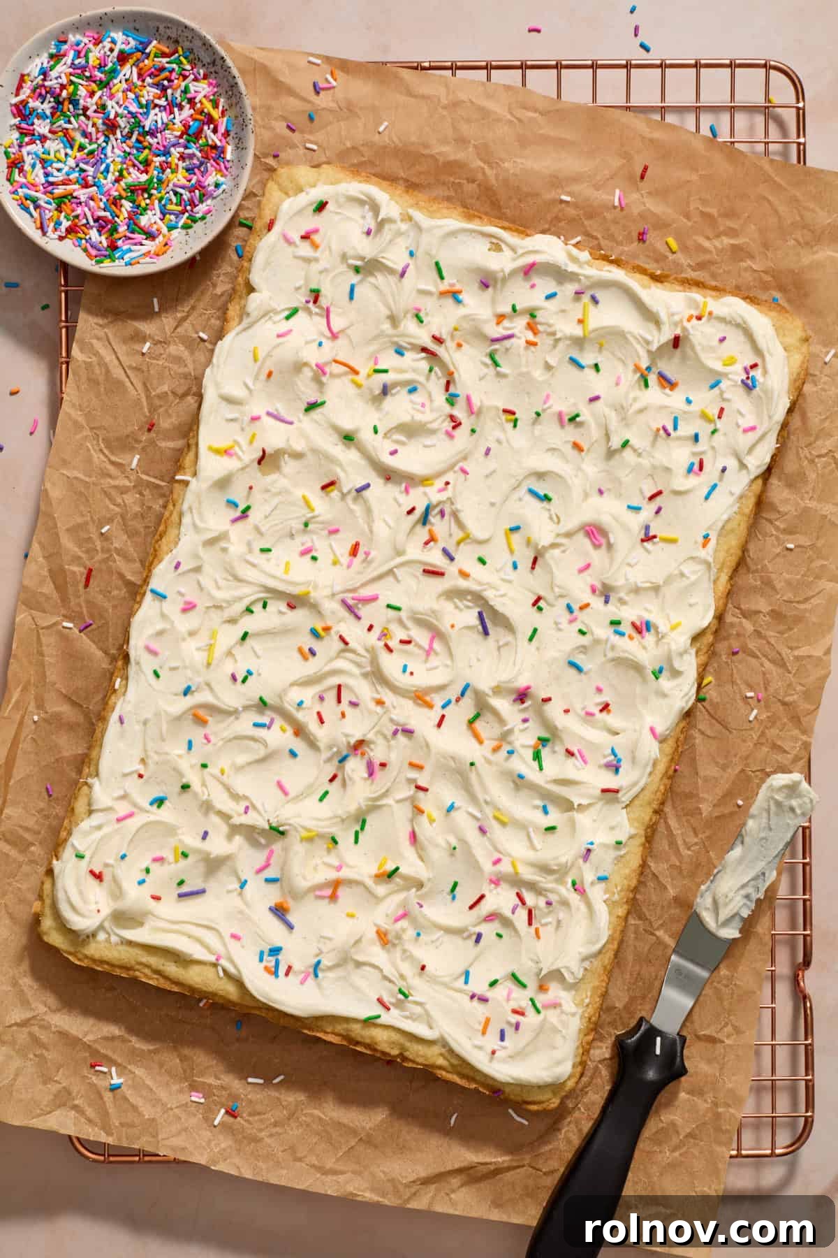 Beautifully frosted sugar cookie bars, topped with a cascade of colorful sprinkles, resting on parchment paper.
