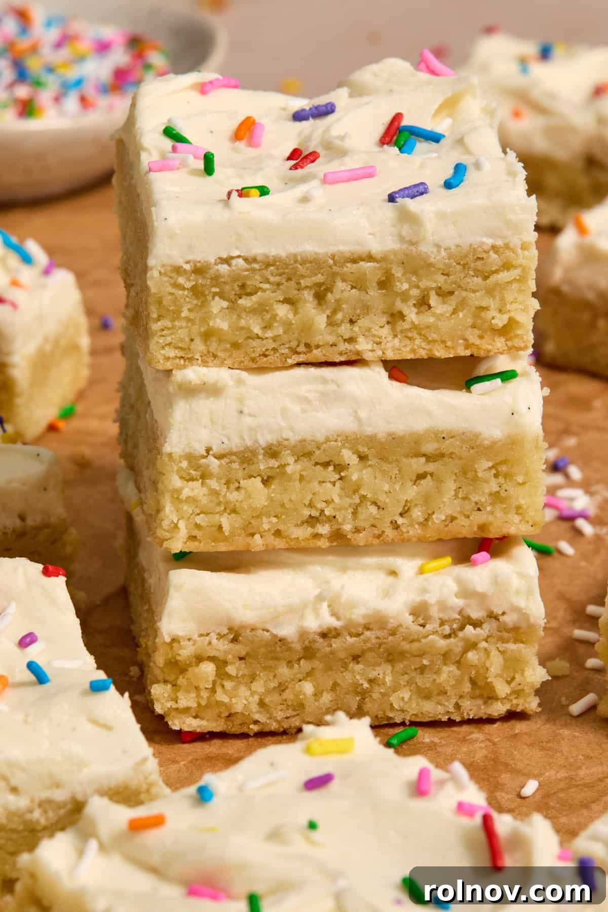 A neatly stacked trio of frosted sugar cookie bars, generously adorned with sprinkles, ready to be enjoyed.