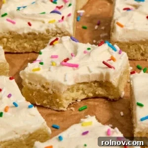 Vanilla bean frosted sugar cookie bars with rainbow sprinkles on parchment.