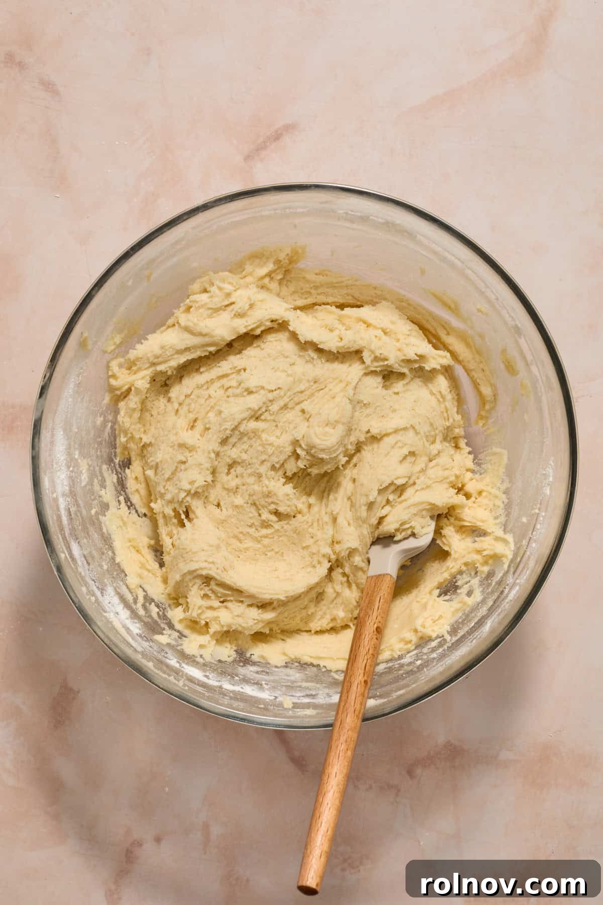 The fully mixed sugar cookie bar dough resting in a bowl, with a spatula demonstrating its soft consistency.