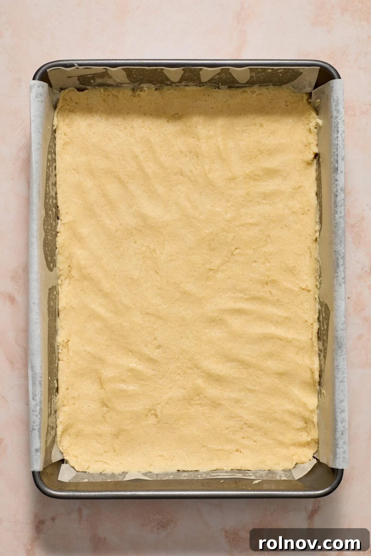 Sticky sugar cookie dough carefully pressed into a parchment-lined 9x13 inch baking sheet, ready for the oven.
