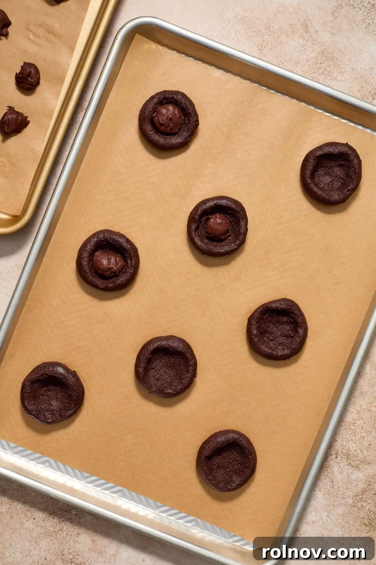 Cookie dough with a thumb indentation, ready for a chocolate ganache piece.