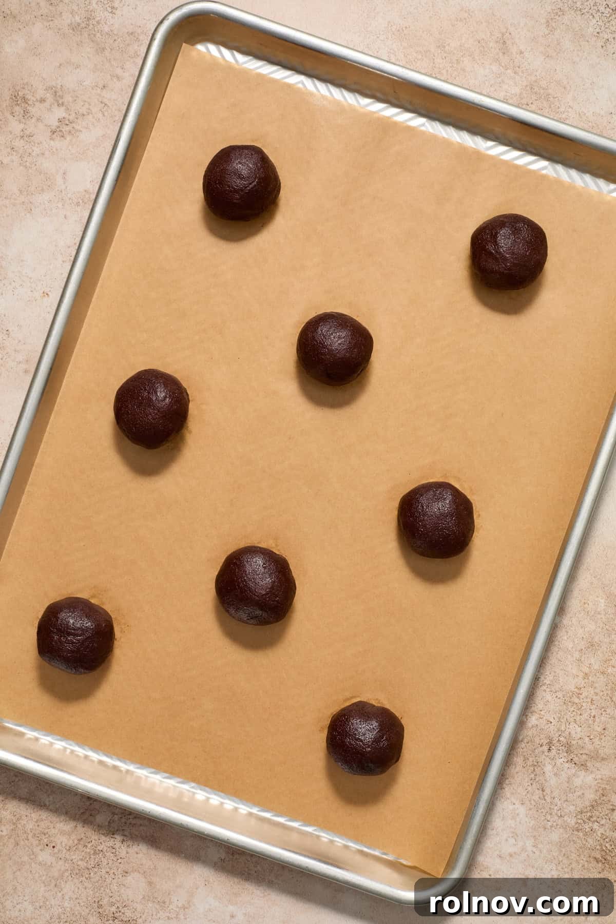 Unbaked chocolate lava cookie dough balls arranged on a parchment-lined baking pan.