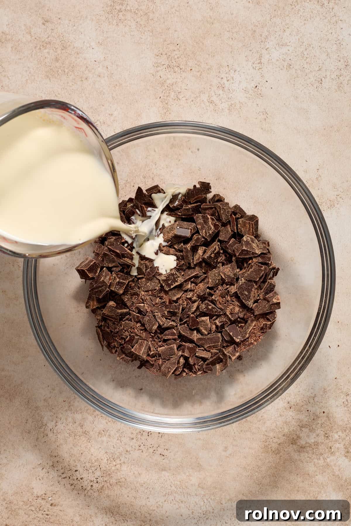 Hot heavy cream being poured over finely chopped chocolate in a bowl.