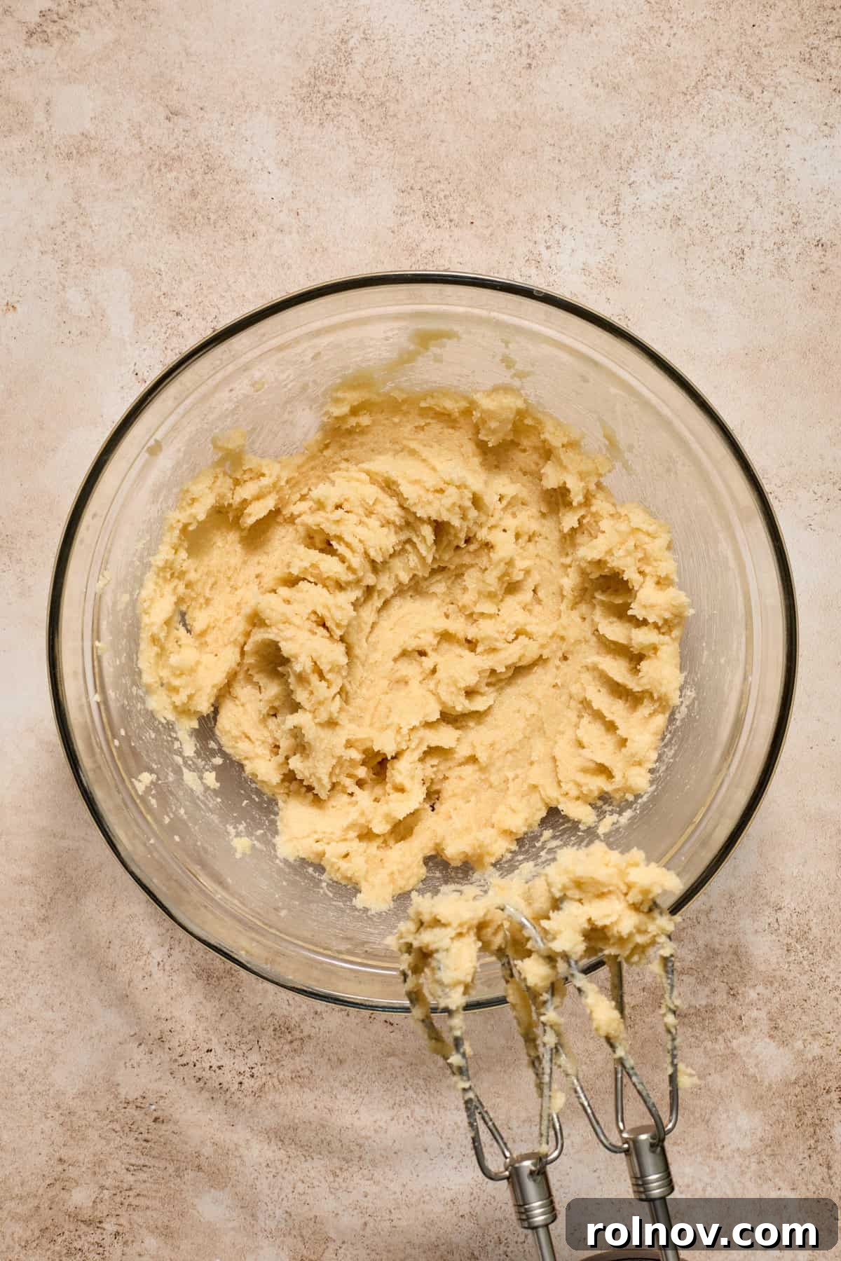 Creamed butter and sugar mixture in a glass bowl, being beaten with a hand mixer.