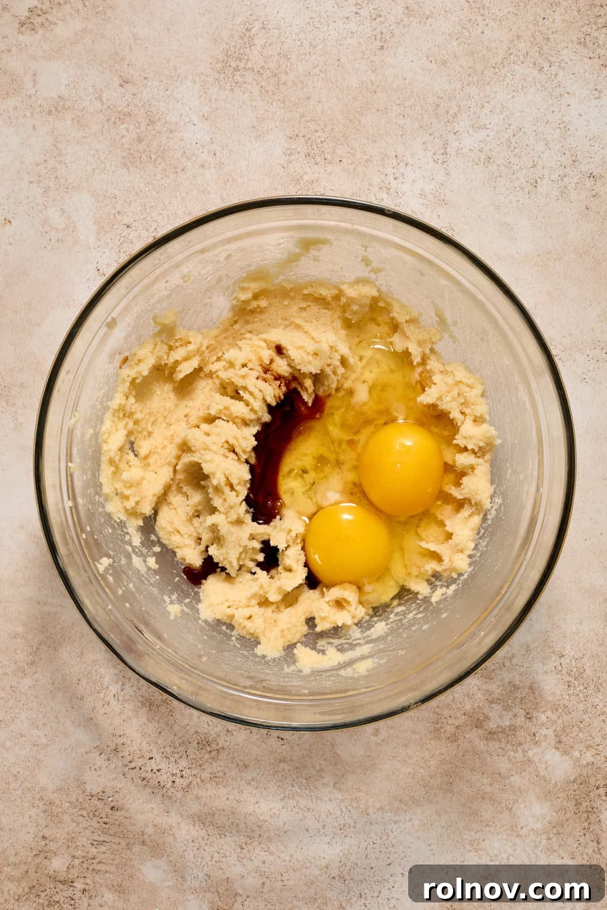 Eggs and vanilla extract added to the creamed butter and sugar mixture in a glass bowl.