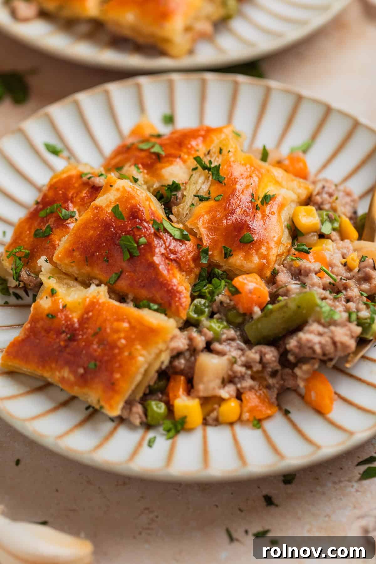 Comforting Ground Turkey Pot Pie 9 A single serving of ground turkey pot pie on a white plate, topped with a couple of puff pastry squares and fresh herbs.