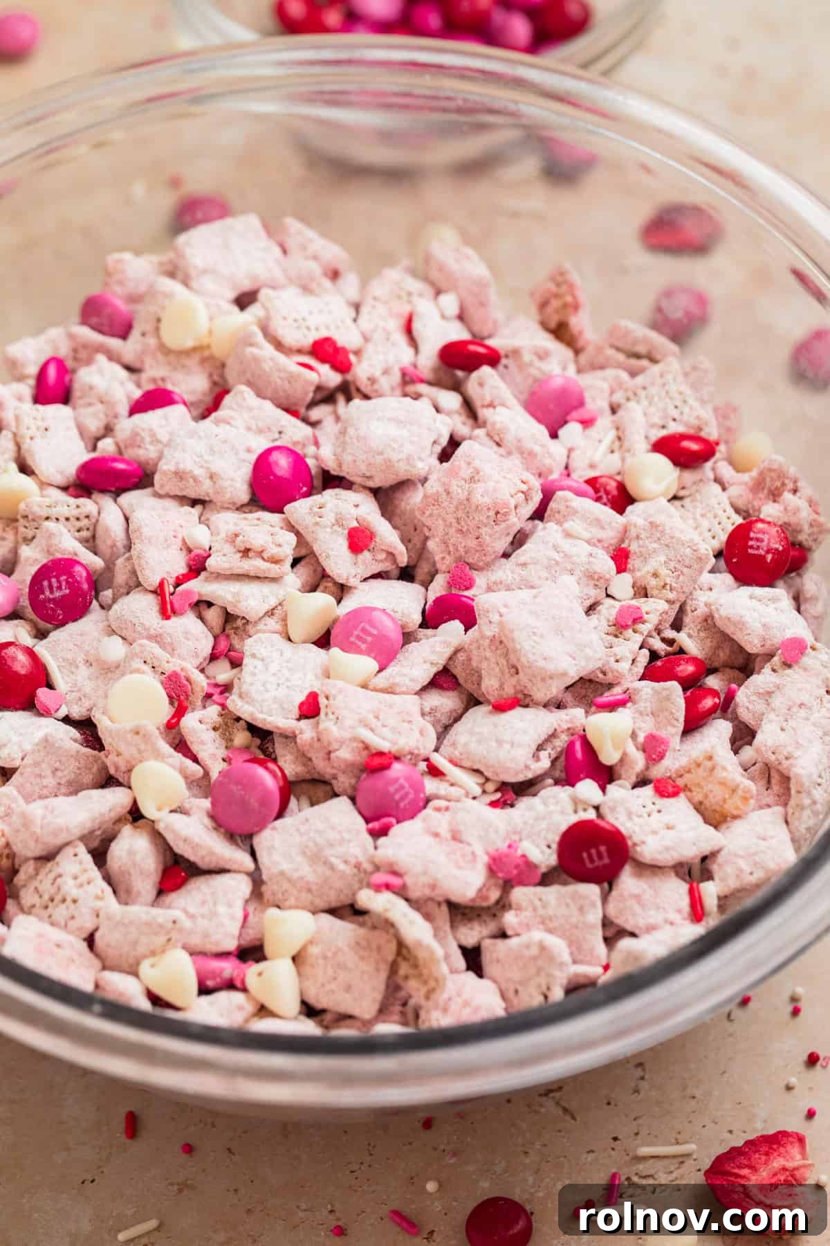 Sweet Strawberry Crunch 2 A bowl of vibrant pink Strawberry Chex Mix, adorned with red and pink M&M candies, perfect for Valentine's Day or any sweet occasion.