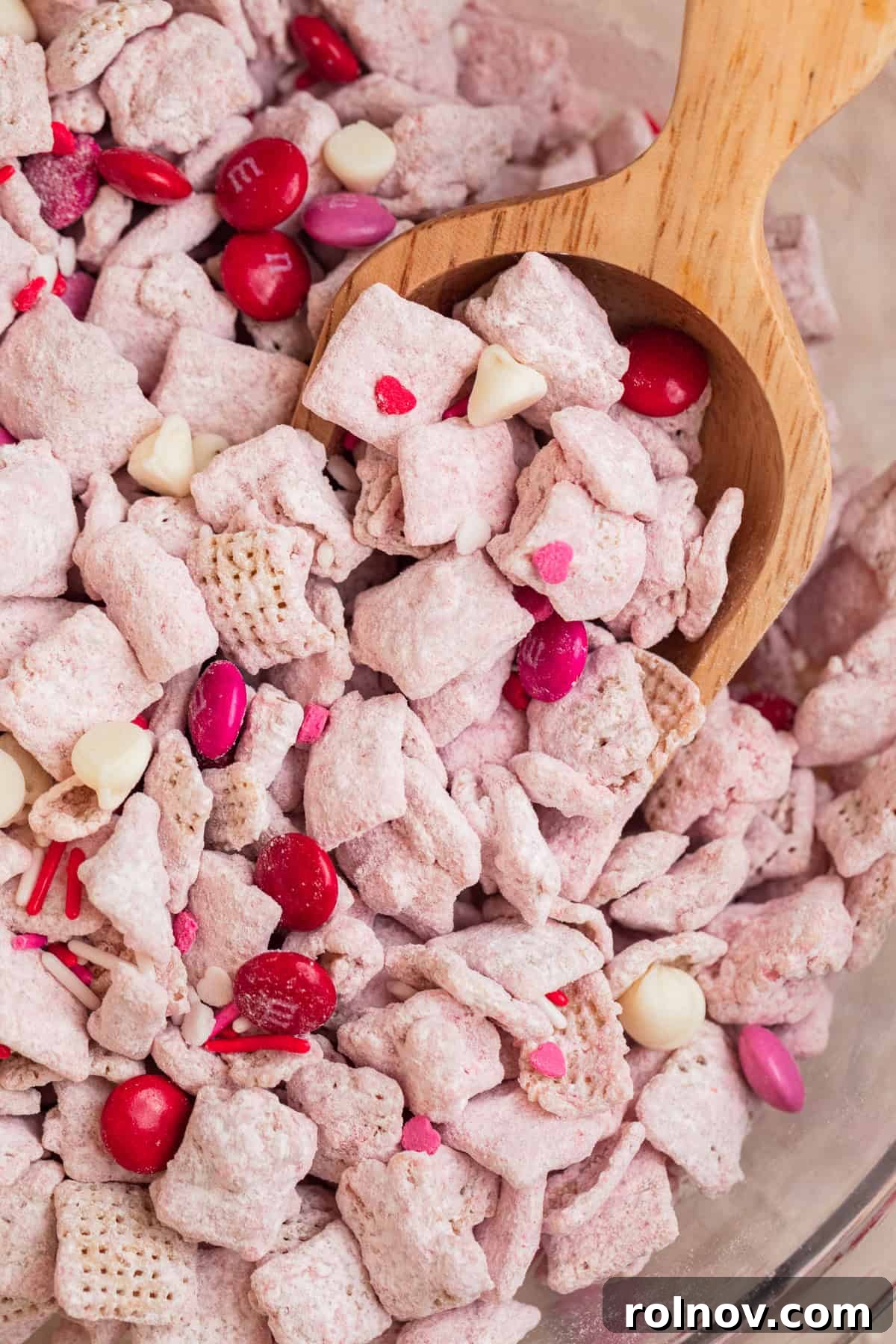 Sweet Strawberry Crunch 13 A large bowl filled with ready-to-eat strawberry puppy chow, with a wooden scoop dipping into the delicious snack.
