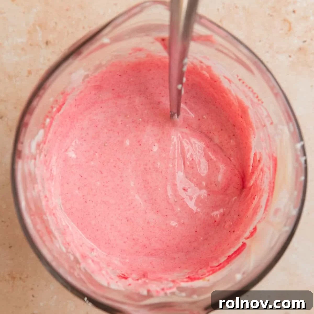 Sweet Strawberry Crunch 7 The vibrant pink melted white chocolate mixture, infused with strawberry, in a glass bowl with a spoon.