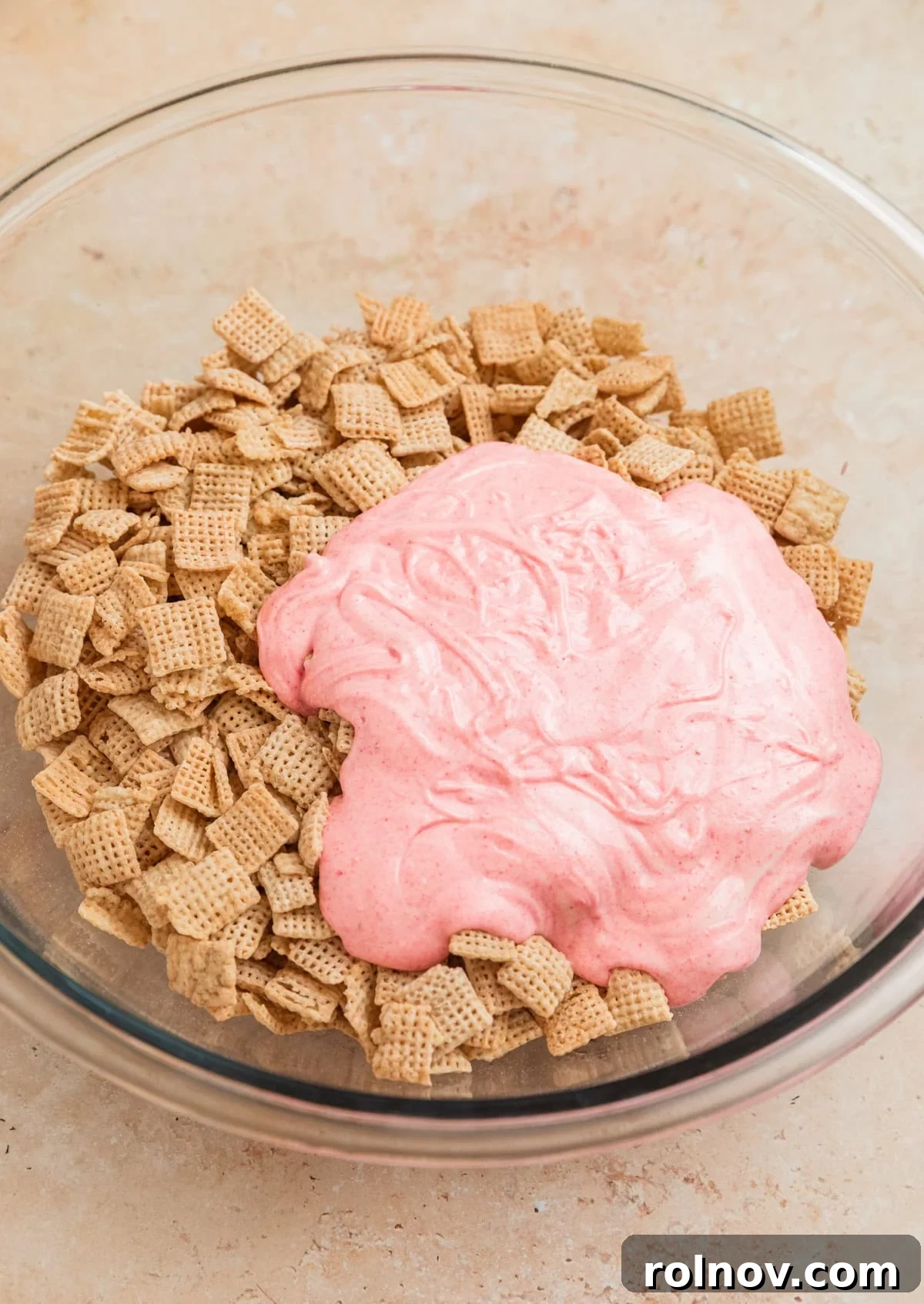 Sweet Strawberry Crunch 8 The strawberry white chocolate mixture being poured generously over rice Chex cereal in a large mixing bowl.