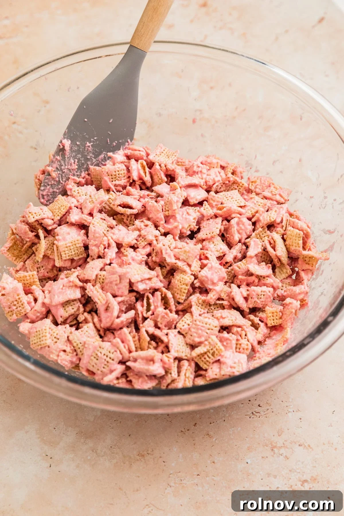 Sweet Strawberry Crunch 9 Strawberry Chex Mix being gently stirred in a bowl to ensure even coating of the cereal.