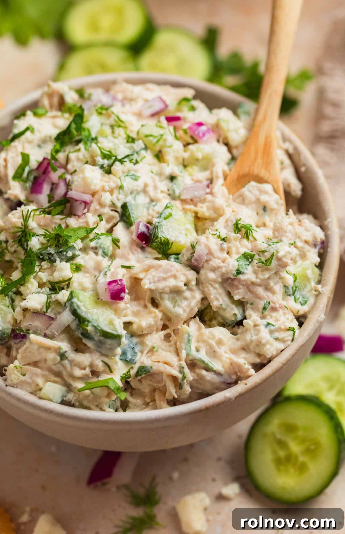 Freshly made feta chicken salad with cucumbers and dill, with a spoon scooping into a serving bowl, ready to be enjoyed.