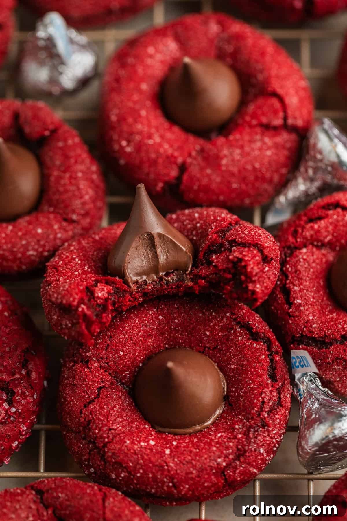 A red velvet cake mix blossom cookie with a bite taken out, resting on a cooling rack with other cookies.