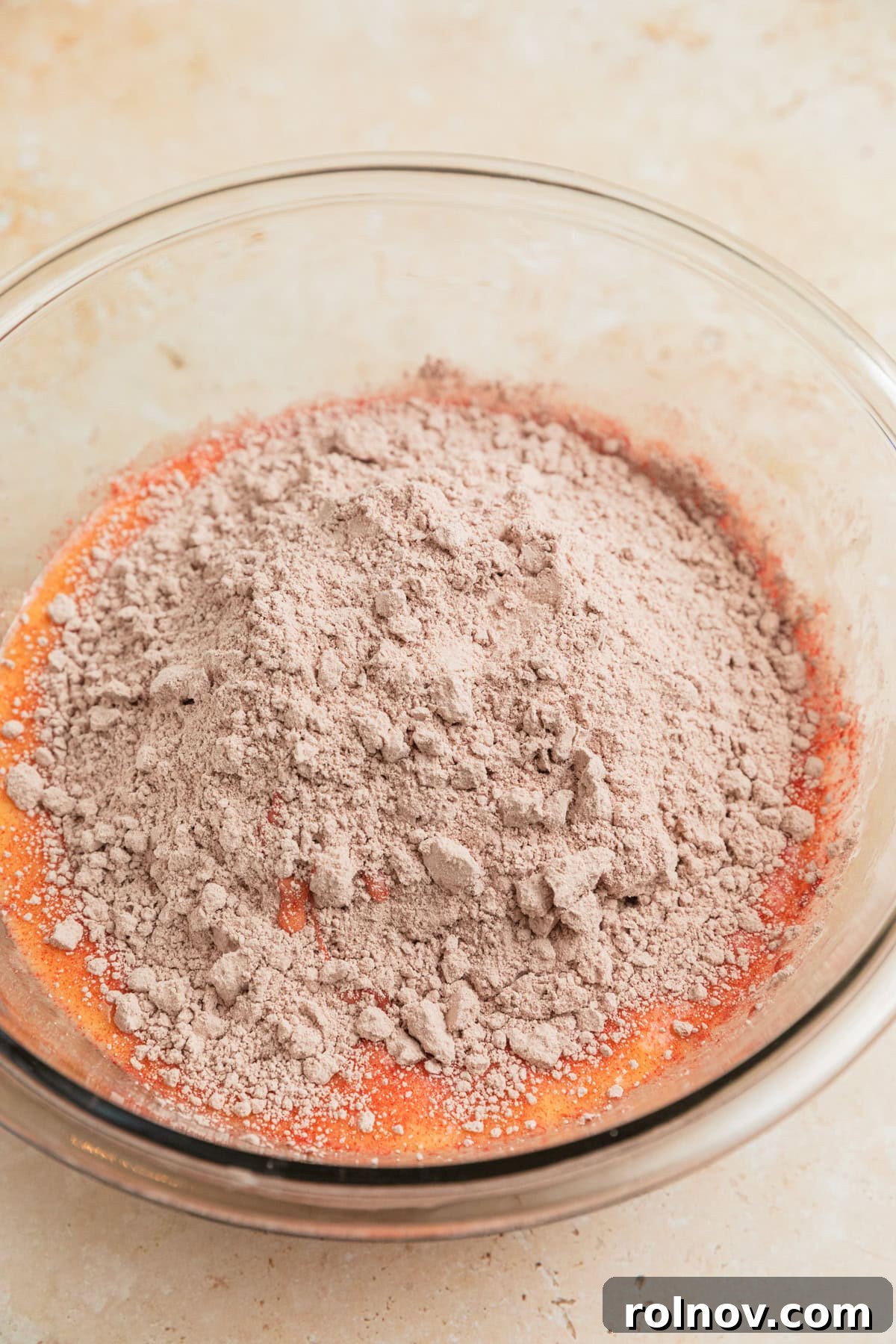 Red velvet cake mix being added to a bowl containing whisked eggs and butter.