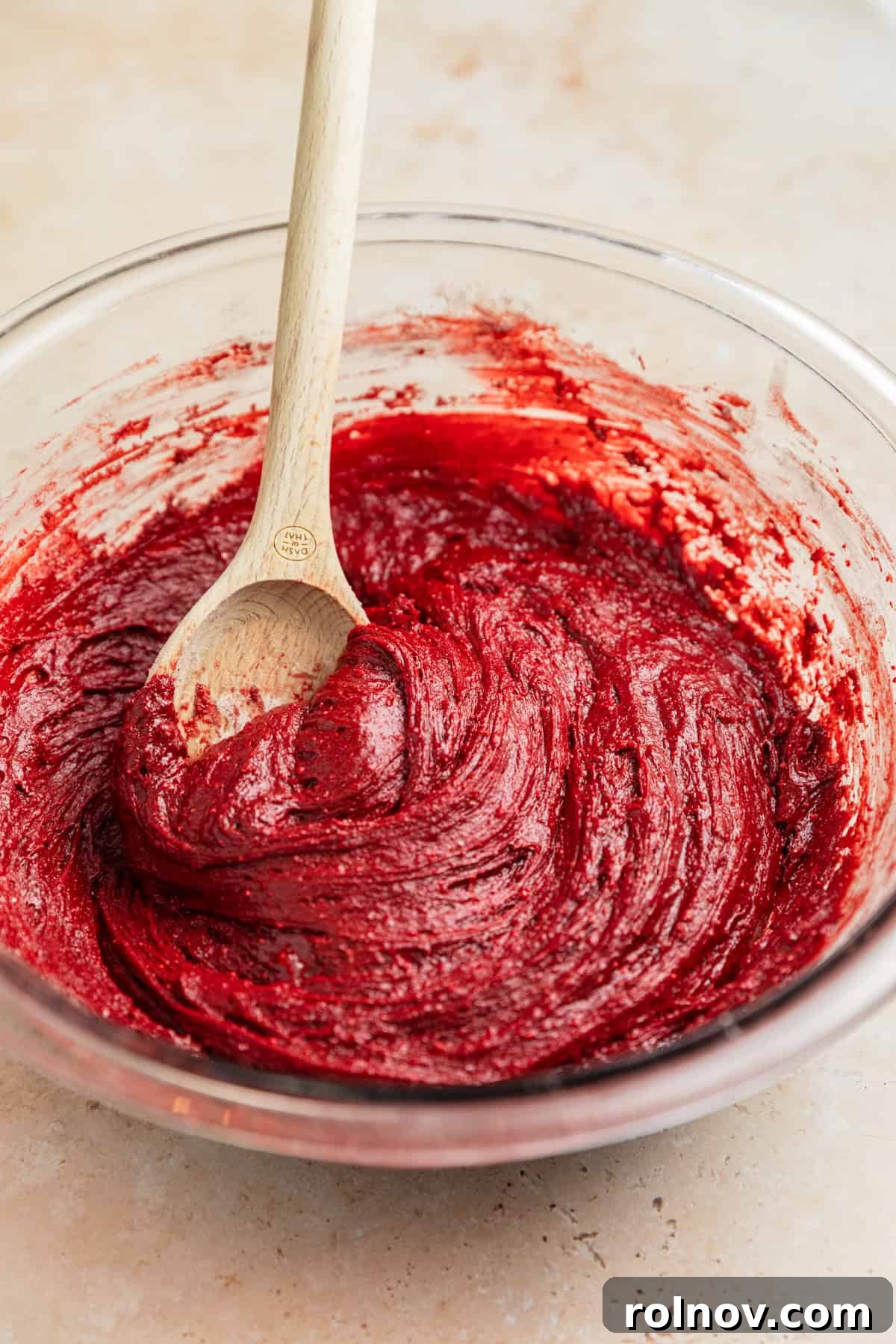 Red velvet cake mix cookie dough resting in a bowl with a wooden spoon.