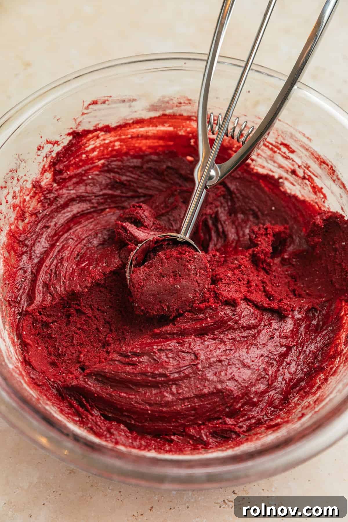 Chilled red velvet cookie dough in a bowl, with a cookie scoop nearby.