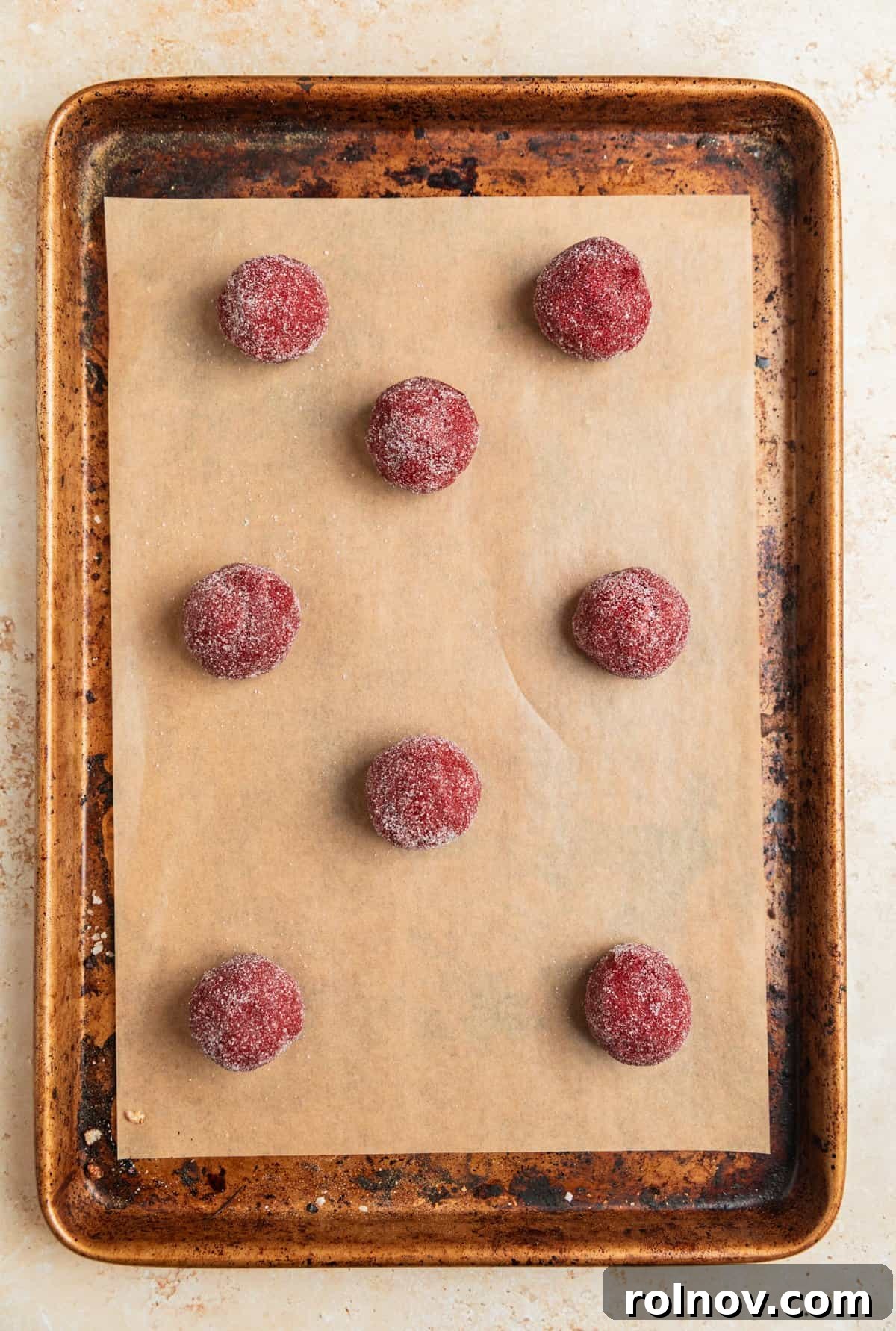 Red velvet cookie dough balls, coated in sugar, arranged on a baking sheet.