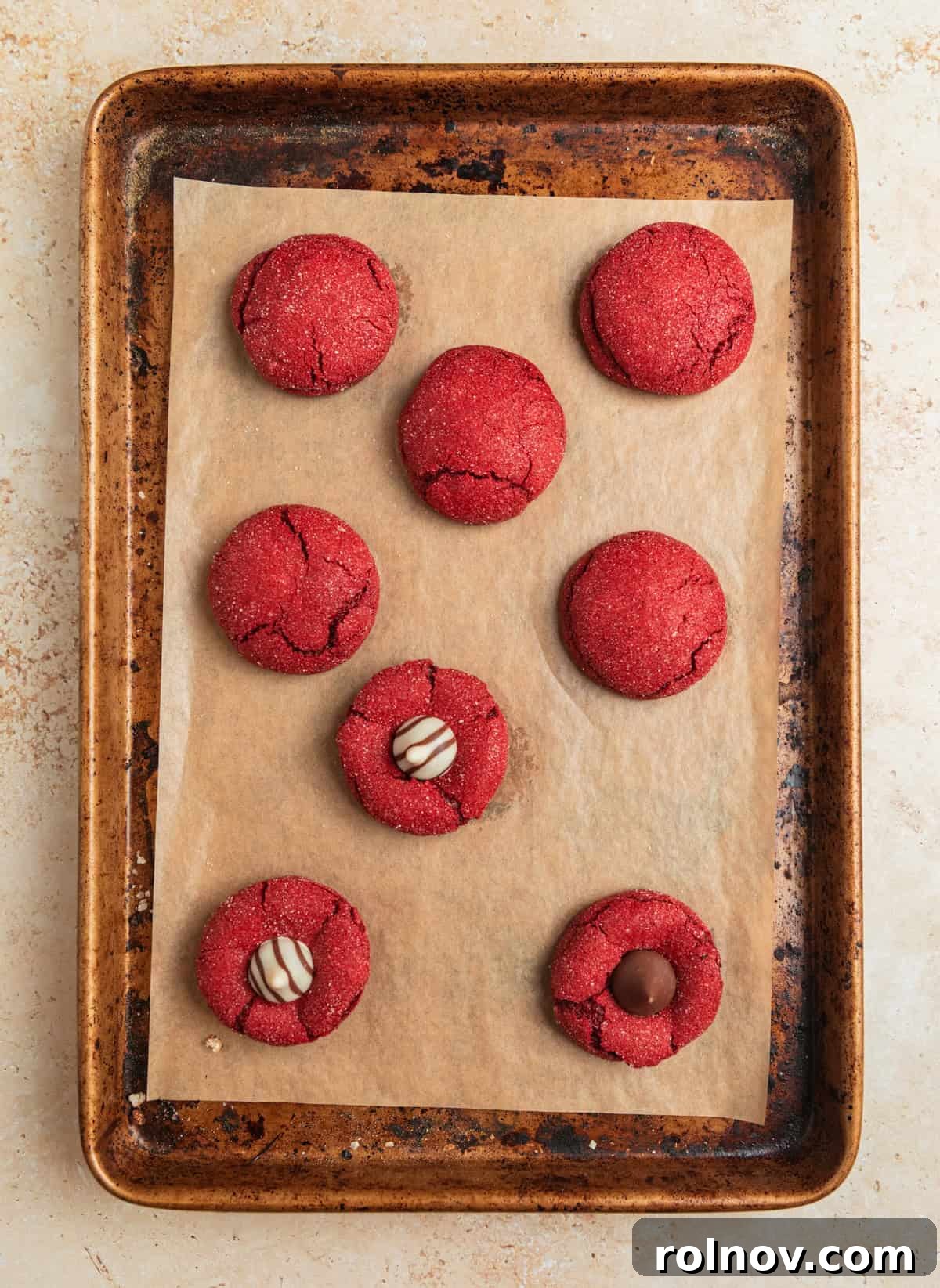 Baked red velvet cookies on a pan, with Hershey's Kisses and Hugs pressed into some of the cookies.