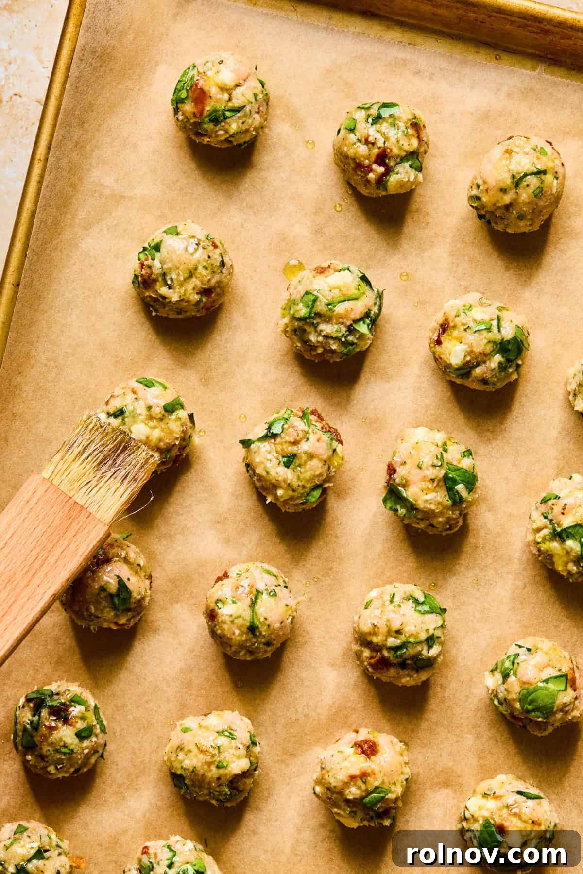 Turkey Meatballs with a Spinach-Feta Swirl 8 Meatballs arranged on parchment lined baking sheet with olive oil being brushed on top.