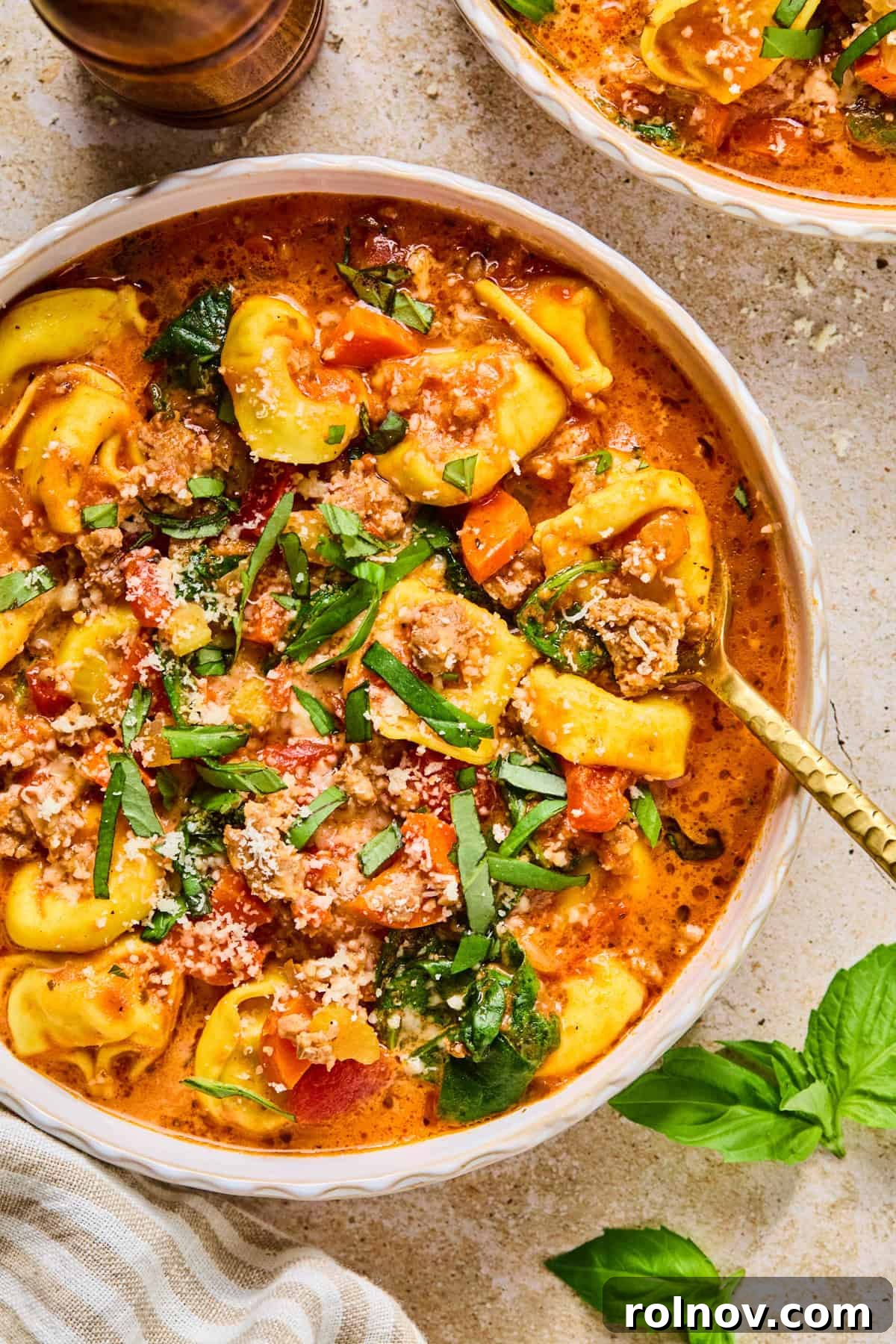 Slow Cooker Creamy Sausage Tortellini Soup 2 A comforting bowl of Crockpot Sausage Tortellini Soup, generously topped with fresh basil leaves, ready to be enjoyed on a cold day.