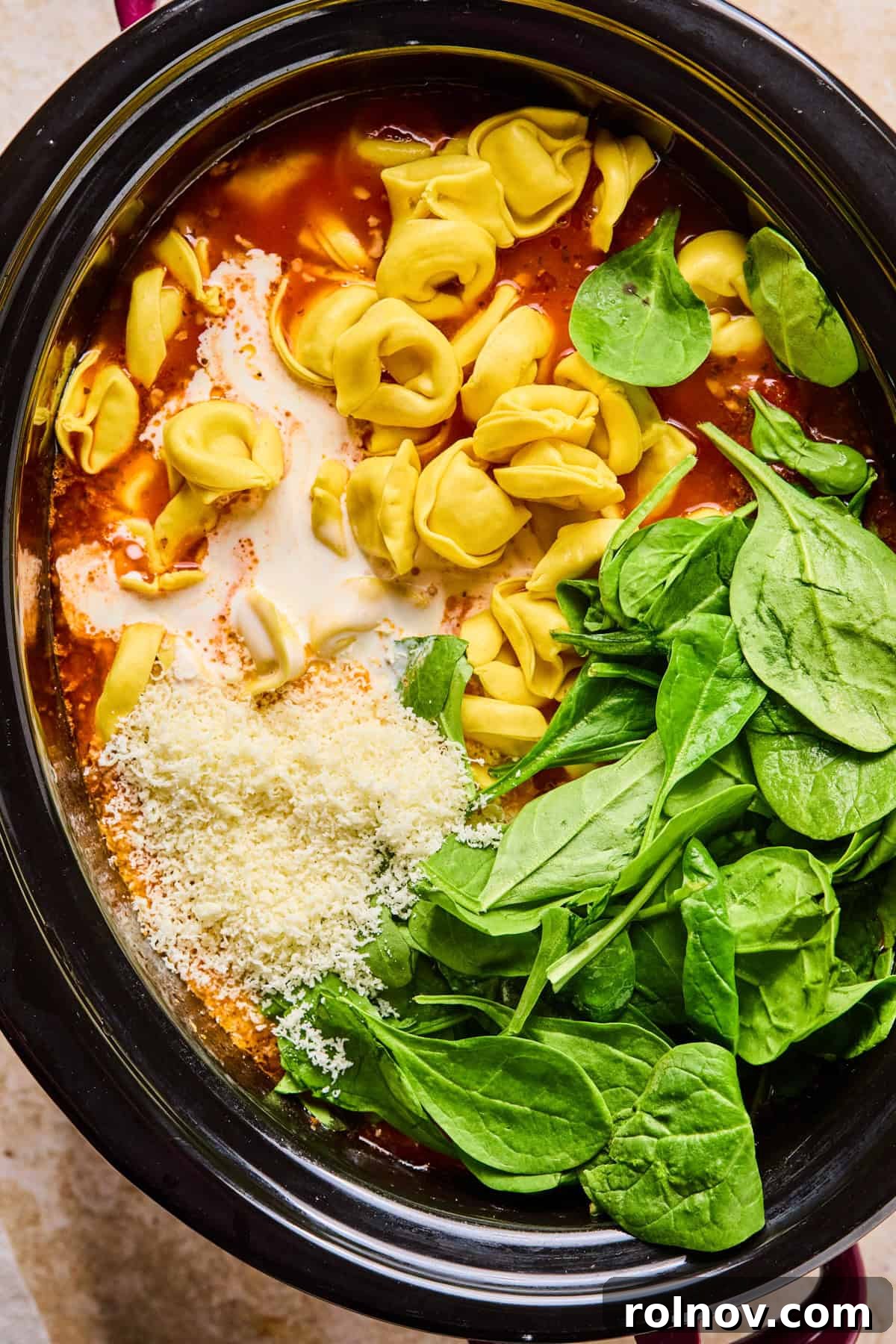 Slow Cooker Creamy Sausage Tortellini Soup 11 Refrigerated tortellini, fresh spinach, heavy cream, and grated Parmesan cheese being added to the cooked soup in the crockpot.
