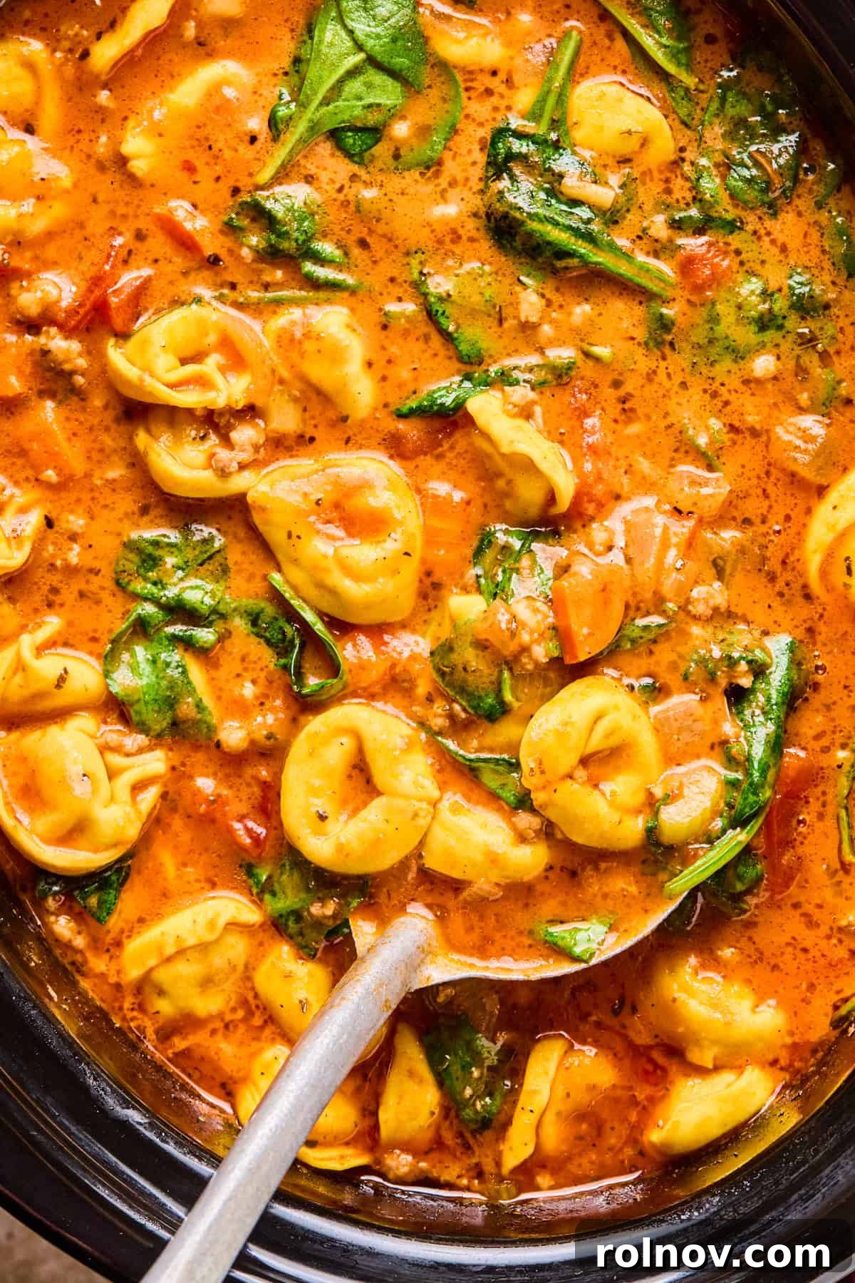 Slow Cooker Creamy Sausage Tortellini Soup 13 A large crockpot brimming with the rich, tomato-based Crockpot Sausage Tortellini Soup, with a ladle poised to serve.