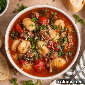 A bowl of rich Italian sausage and gnocchi soup, beautifully topped with fresh herbs and grated Parmesan cheese.