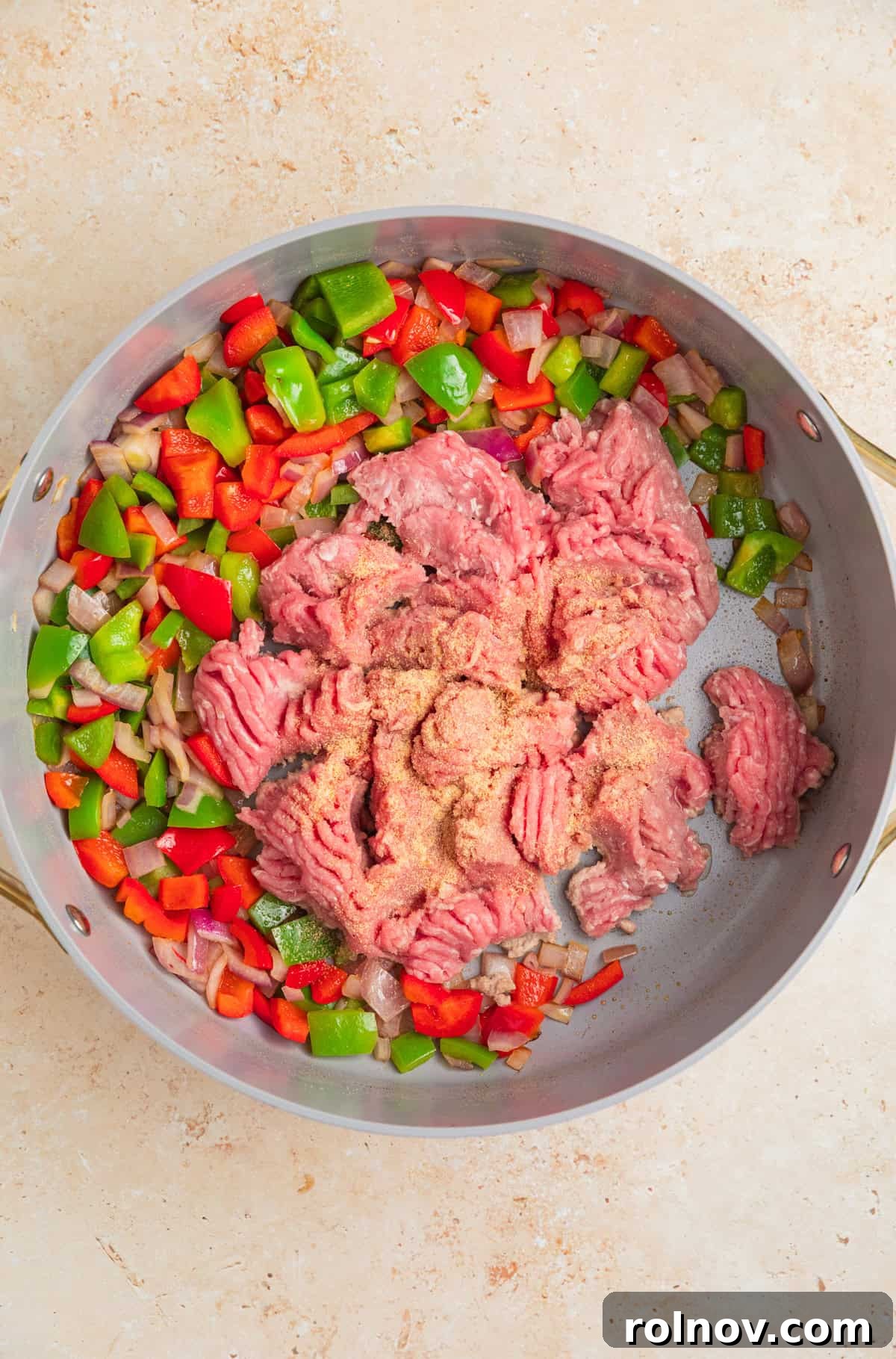 Skillet Turkey Taco Fiesta 5 Ground turkey being added to a hot skillet alongside sautéed onions and bell peppers, ready to be cooked.