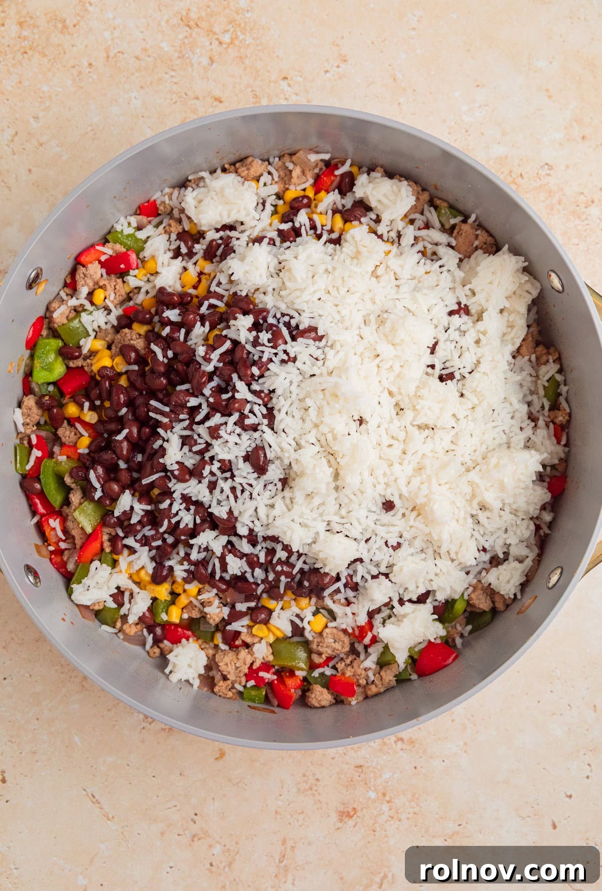 Skillet Turkey Taco Fiesta 7 All the main ingredients, including cooked rice, black beans, diced tomatoes, and corn, being added to the browned turkey mixture in the skillet.