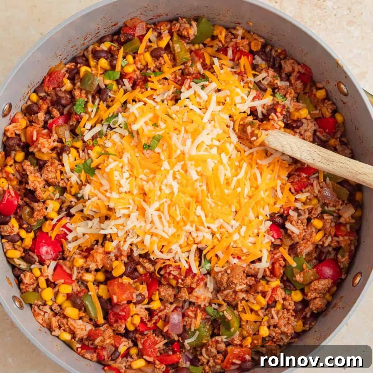 Skillet Turkey Taco Fiesta 8 Shredded cheddar cheese being stirred into the hot ground turkey and rice taco mixture in the skillet, creating a creamy texture.