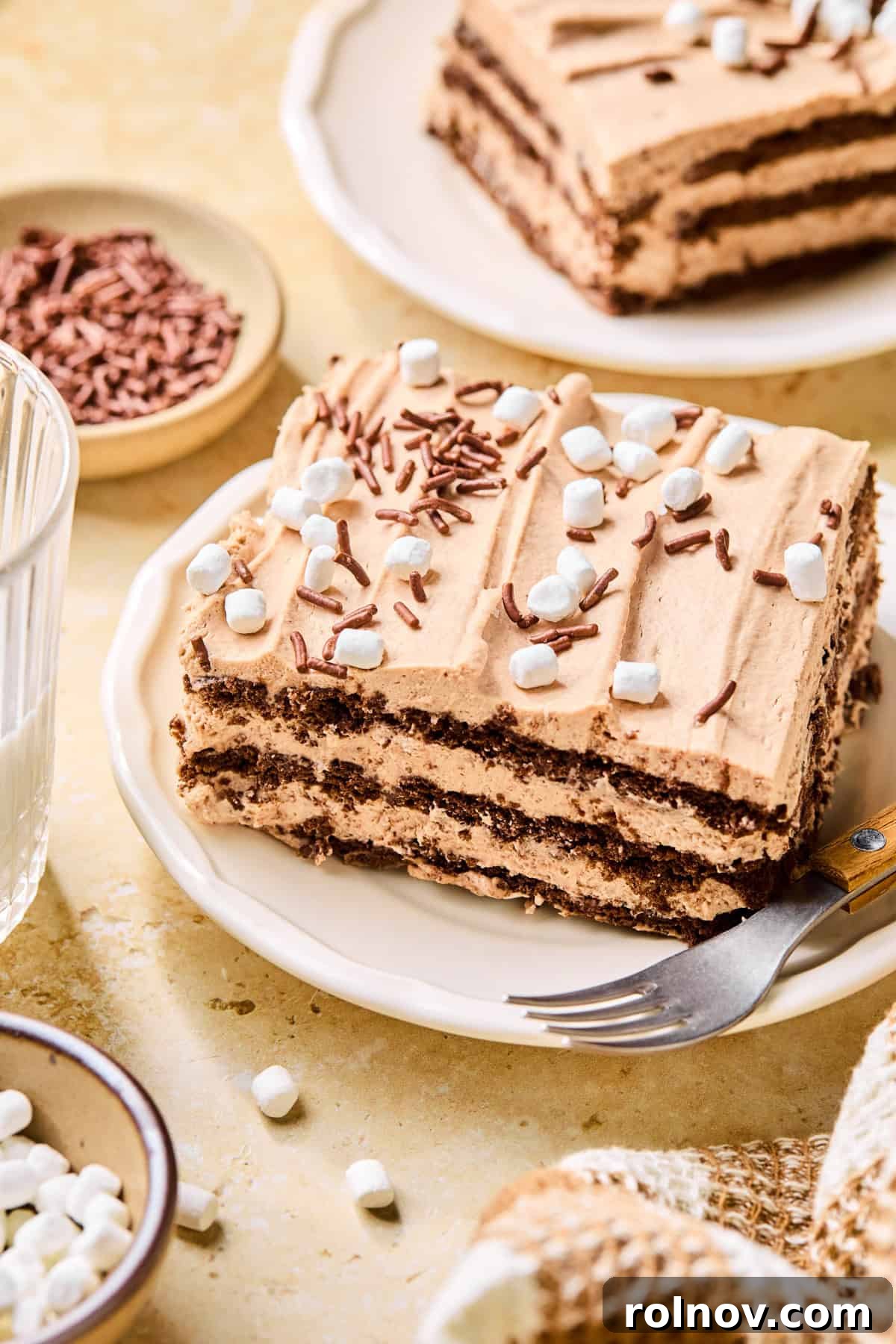 Decadent No-Bake Chocolate Cake 2 A perfectly sliced Hot Chocolate Icebox Cake on a plate, garnished with chocolate sprinkles and miniature marshmallows, ready to be enjoyed with a fork.