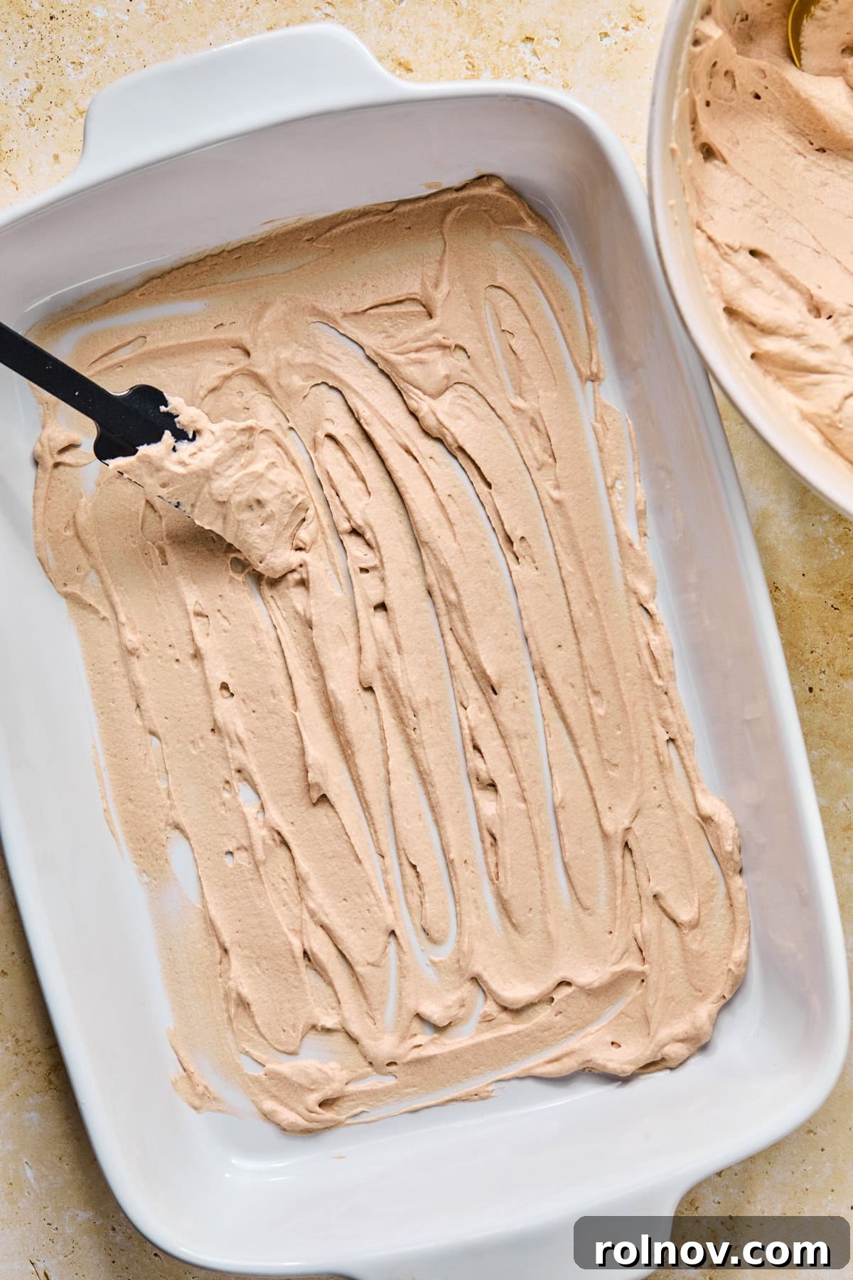 Decadent No-Bake Chocolate Cake 11 A thin layer of chocolate whipped cream mixture being spread evenly on the bottom of a 9x13 inch baking pan with a spatula.