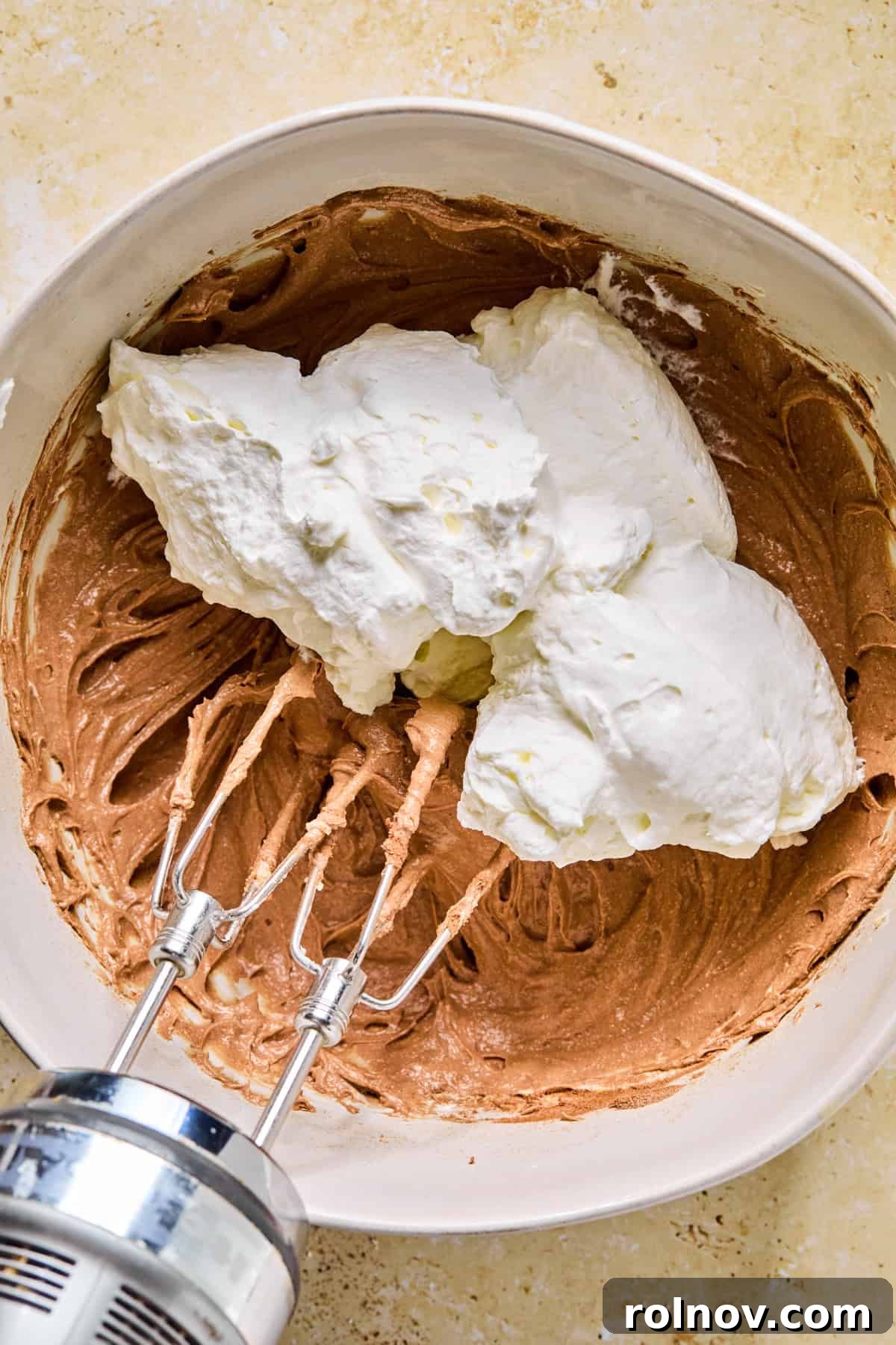 Decadent No-Bake Chocolate Cake 8 Dollops of fluffy whipped cream added to the chocolate cocoa cream cheese mixture in a mixing bowl.