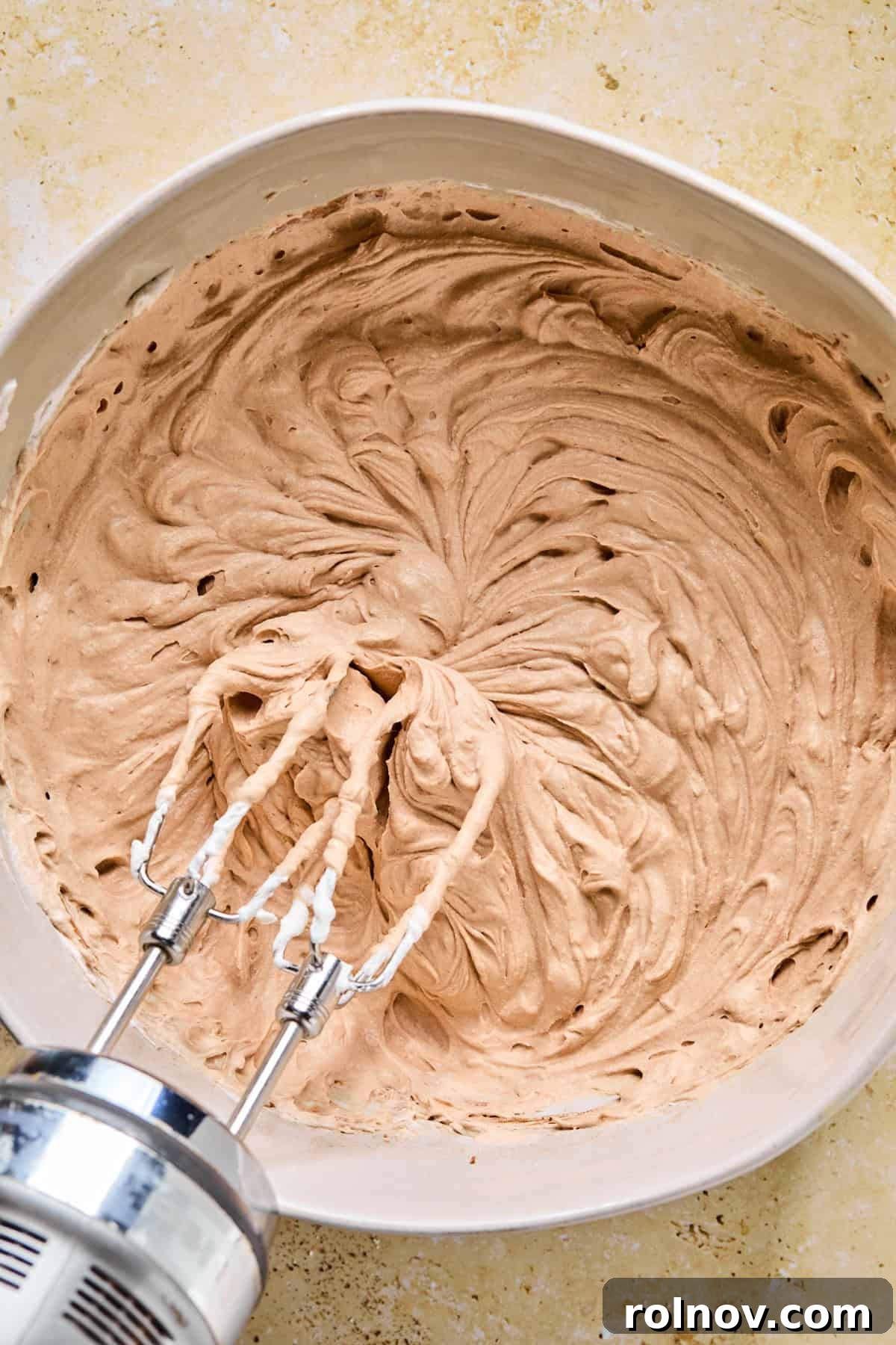 Decadent No-Bake Chocolate Cake 9 The chocolate whipped cream mixture in a bowl with an electric mixer propped above, showing initial mixing.